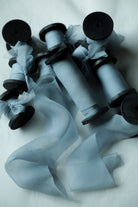 A set of light blue sheer organza ribbon spools on black wood spools, arranged on a white fabric background.