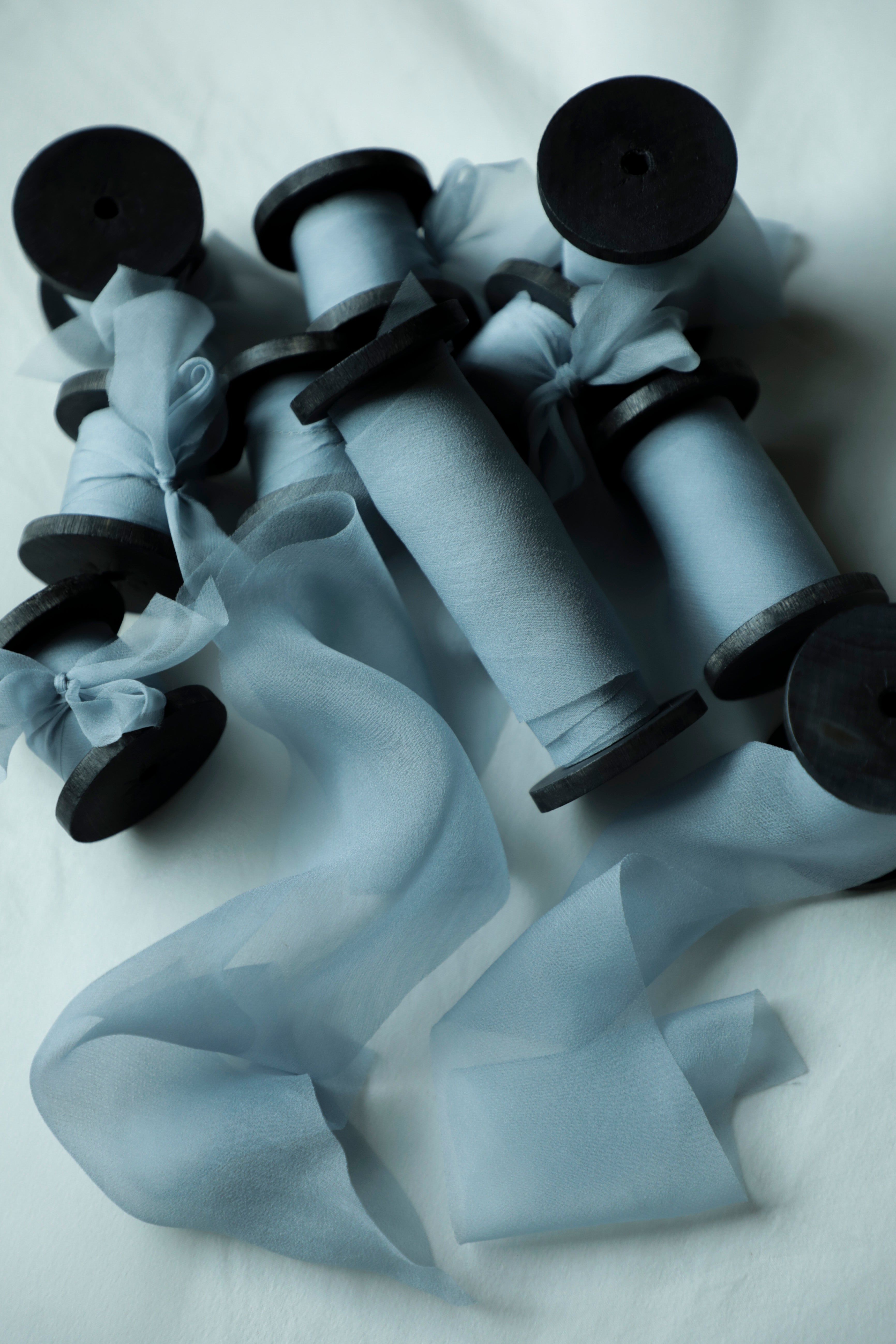 A set of light blue sheer organza ribbon spools on black wood spools, arranged on a white fabric background.