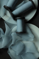 Light blue sheer silk ribbons draped over white circular plates, photographed in moody low light on a dark surface.