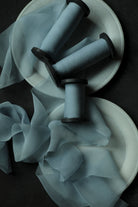 Three light blue organza ribbon spools with black wood spools, arranged on white plates with draped blue ribbon against a dark background.