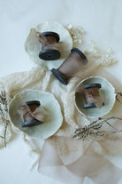 Three vintage-style black wood spools of ribbon, wrapped in coral organza silk ribbon, arranged on a white surface with a cream lace cloth and dried floral accents.