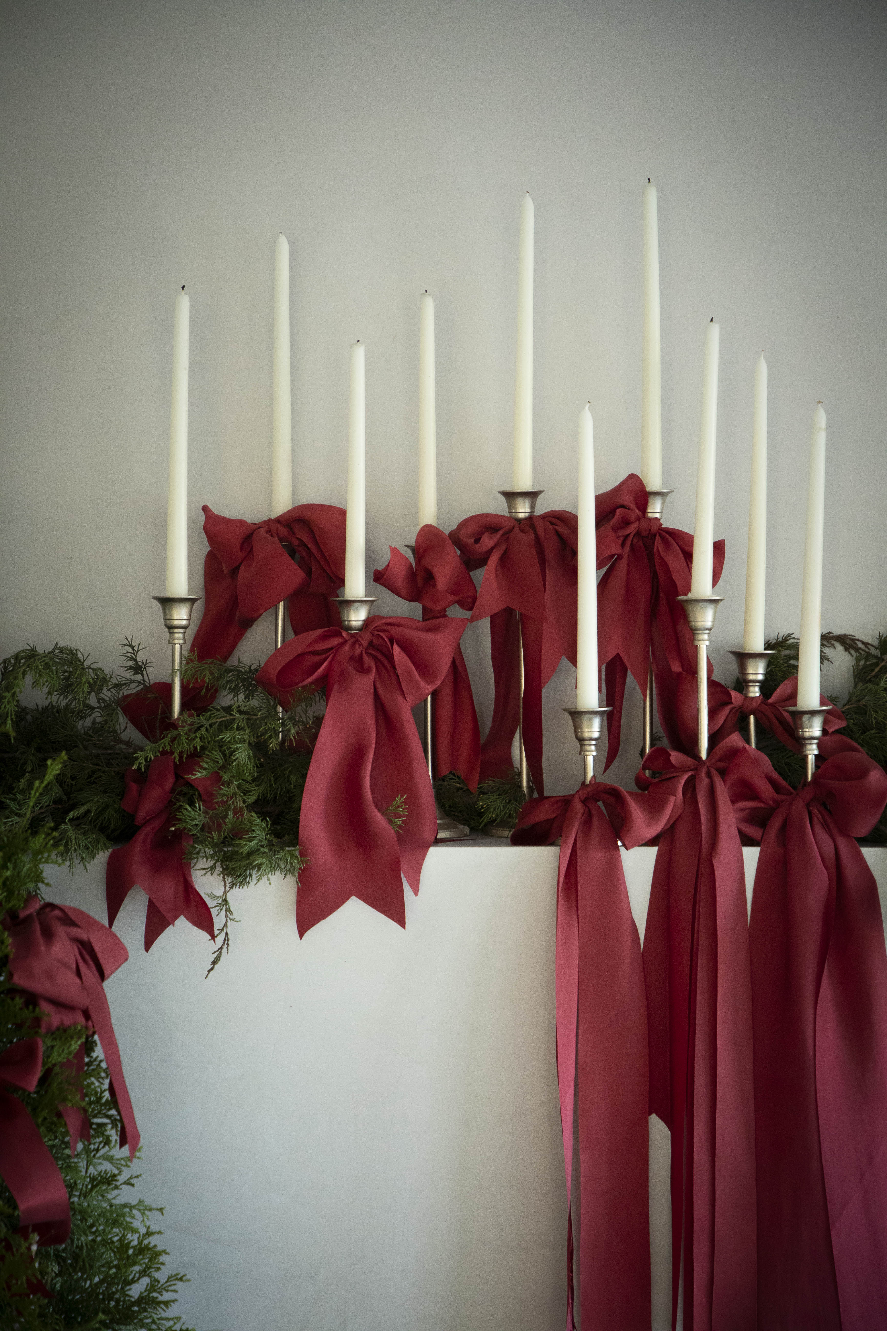 chrismas mantel display with candles and red ribbons with winter greenery for a elevated christmas display. 