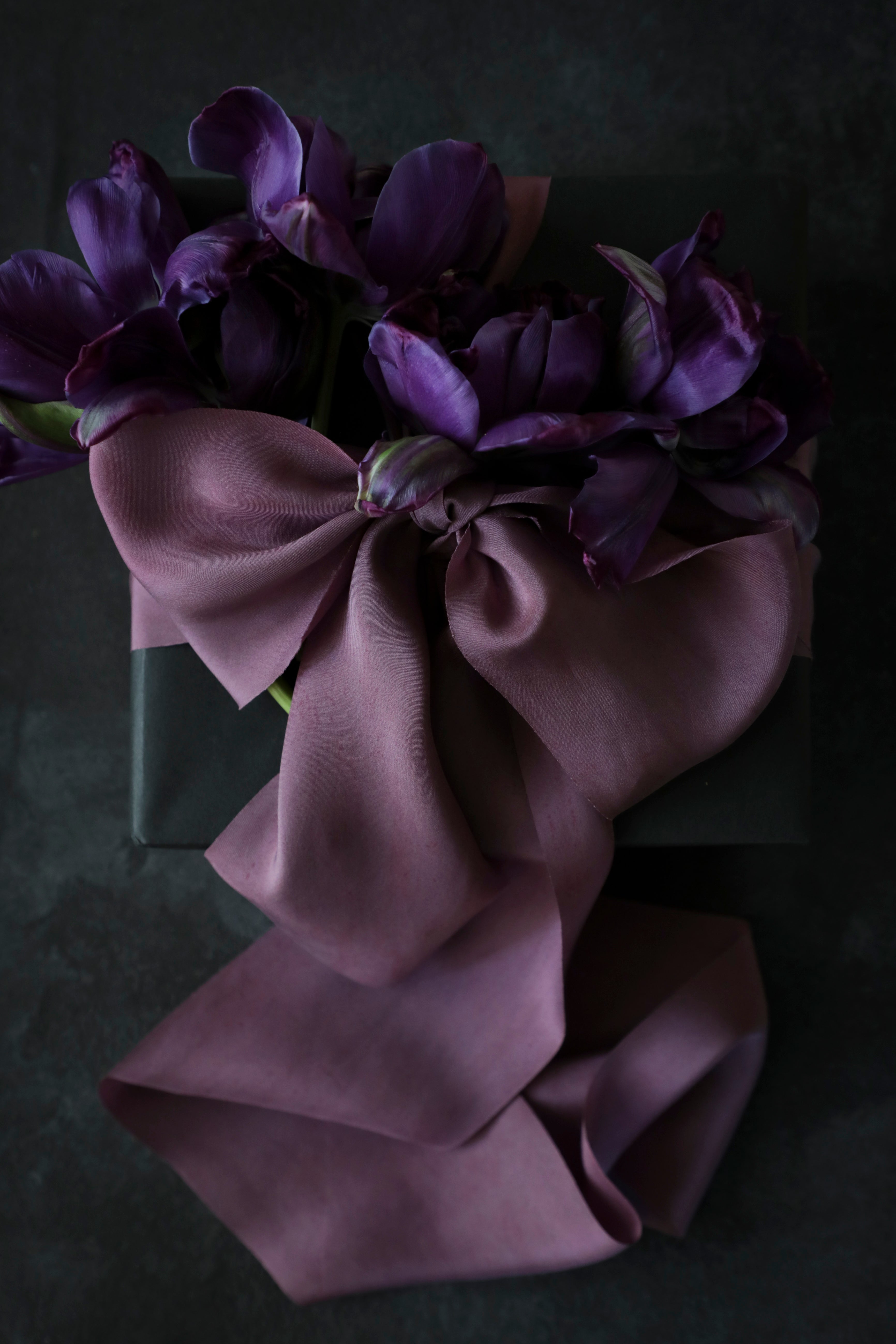 Unique gift wrapping inspiration. gift wrapping with purple silk ribbon bow against a textured black back ground