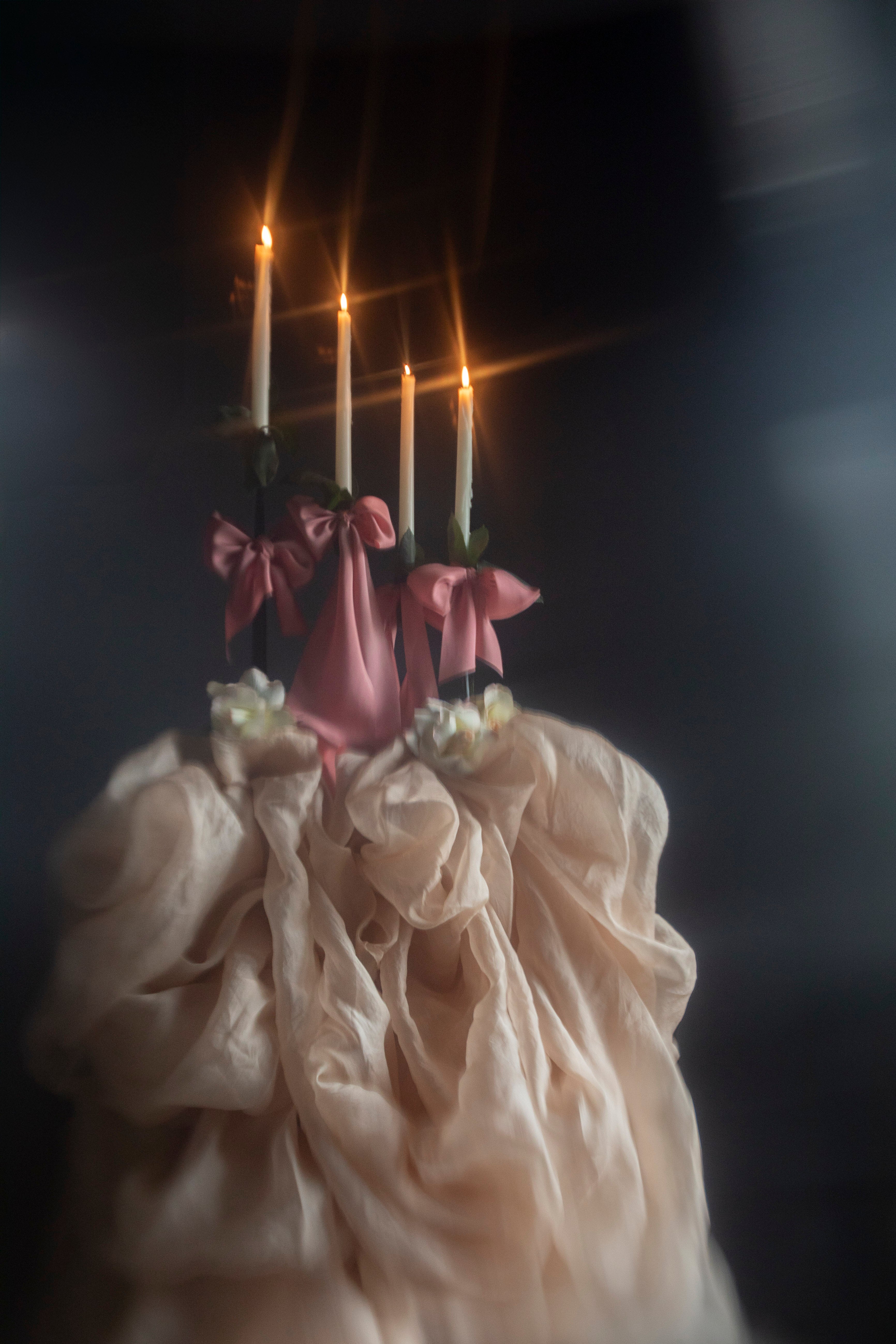 Decorative object with candles and pink ribbons against a dark background
