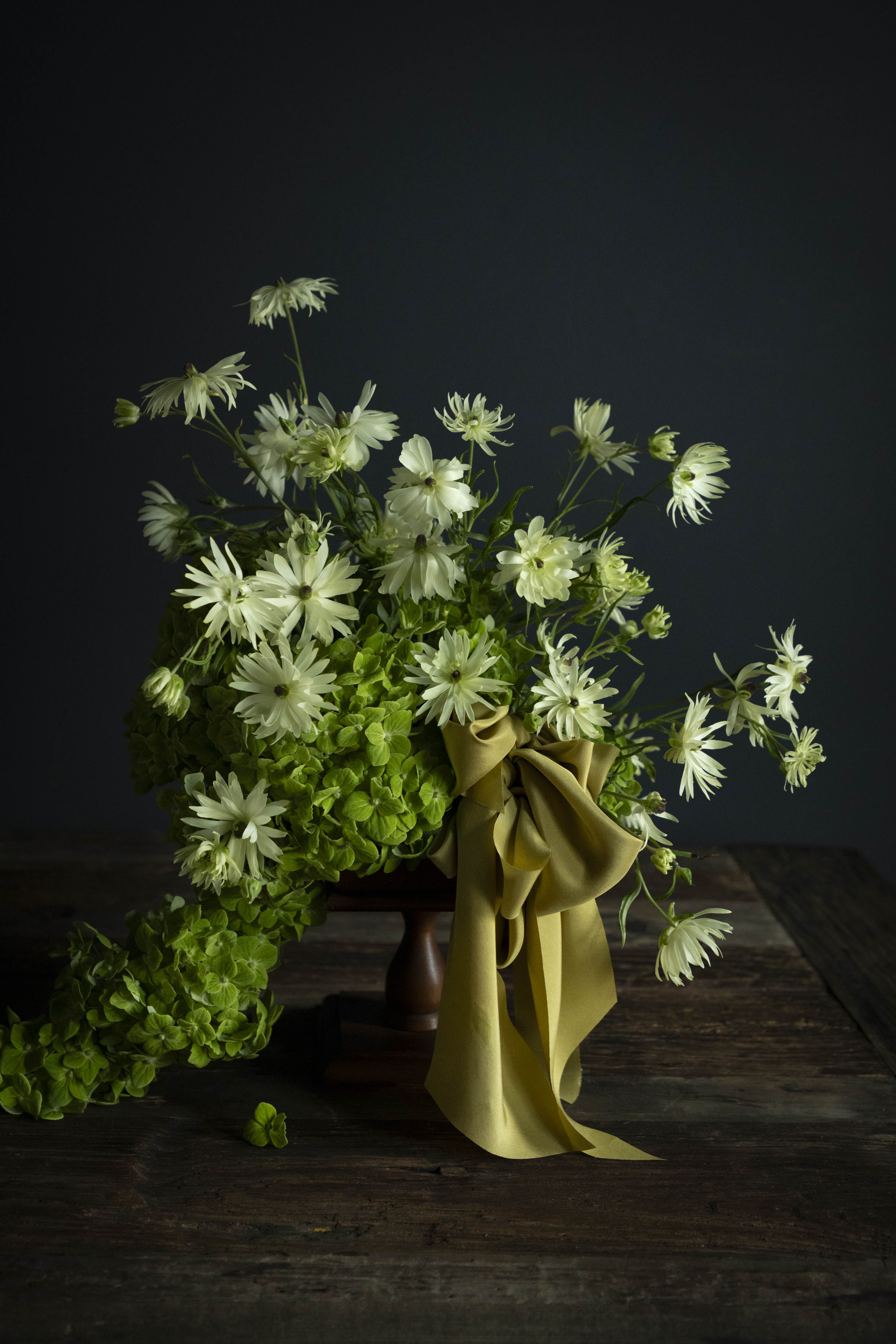 Bouquet of white flowers with greenery on a dark background. A cirtus green ribbon bow adorns the arrangement