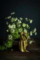 Bouquet of white flowers with greenery on a dark background. A cirtus green ribbon bow adorns the arrangement