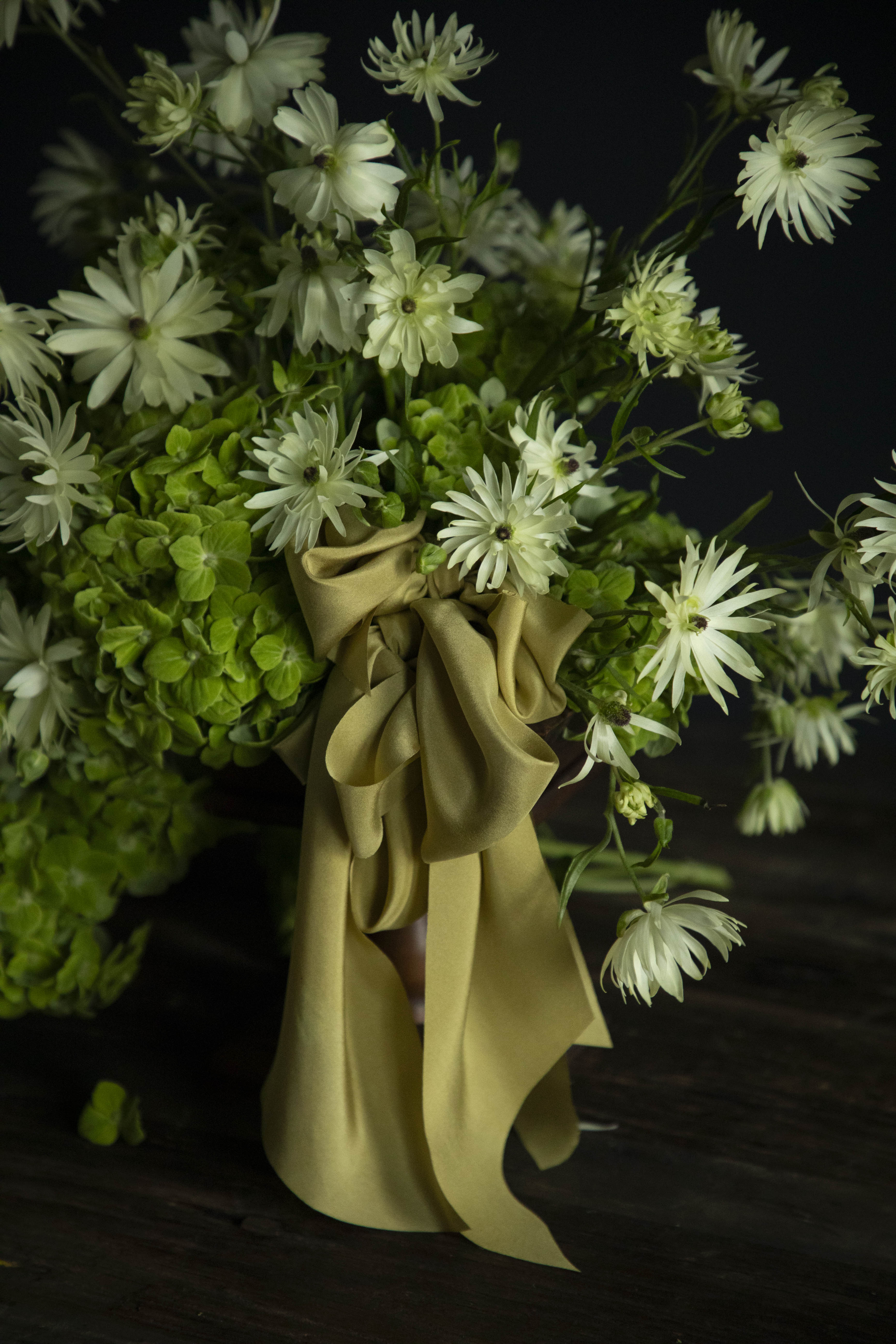 Bouquet of green and white flowers with a Chartreuse yellow ribbon on a dark background