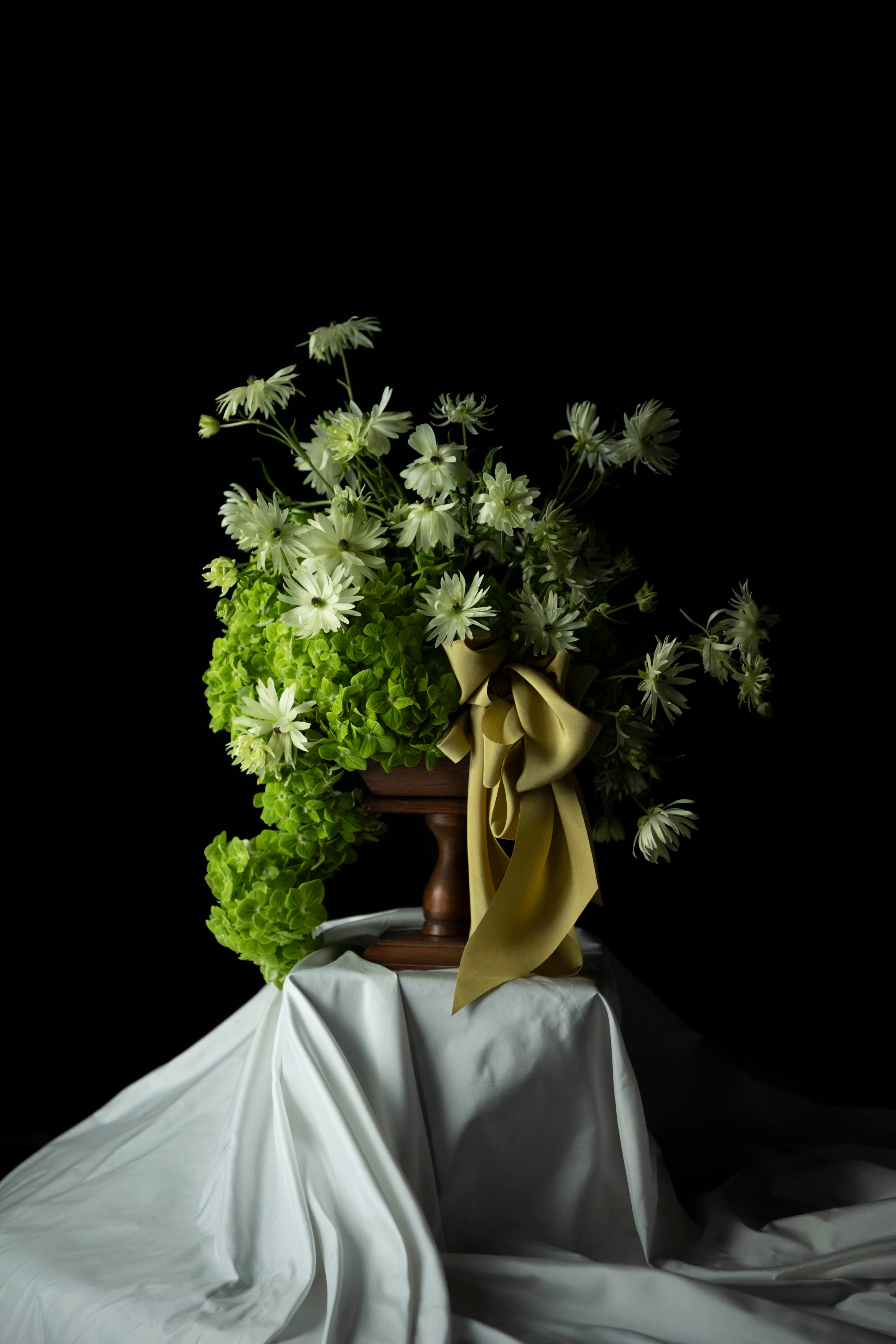 Bouquet of flowers with a green ribbon on a white tablecloth against a black background