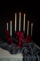 Candles display draped with red ribbon bows on layered gray table textiles against a dark background