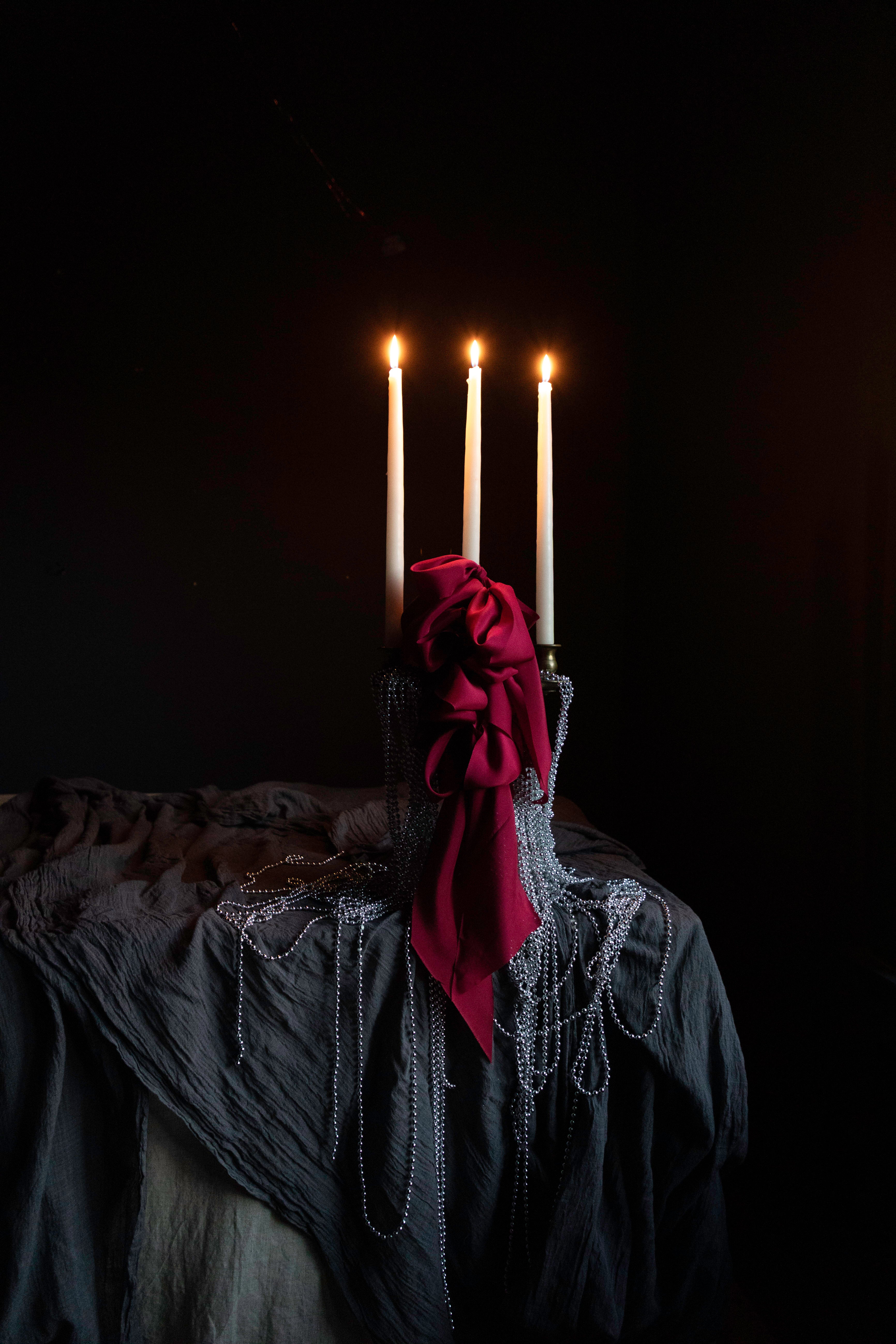 candles draped with metal beads and red ribbon bows on layered gray table textiles against a dark background