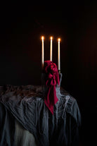 candles draped with metal beads and red ribbon bows on layered gray table textiles against a dark background