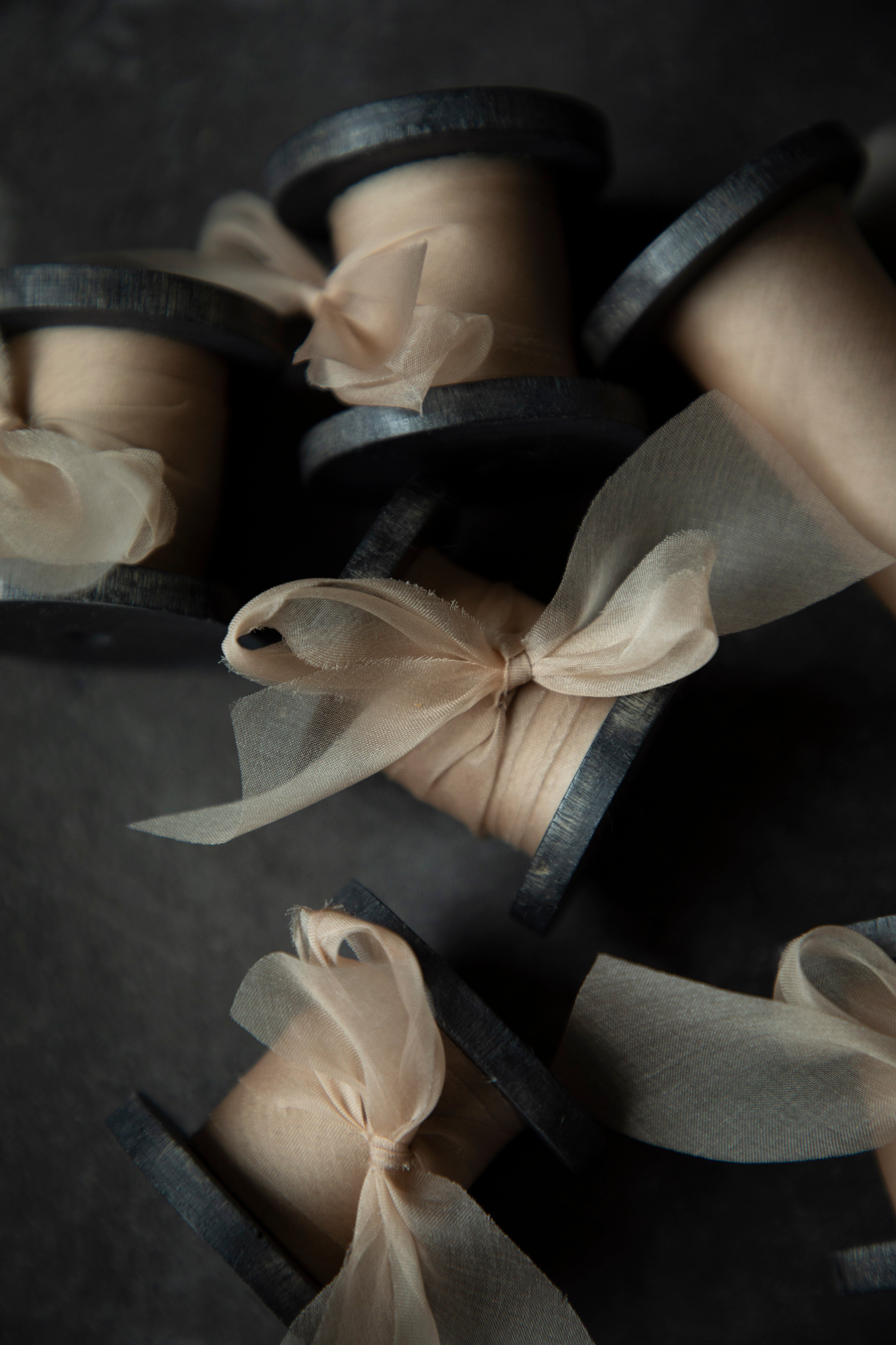 Spools of beige ribbon tied into bows on dark wooden spools.