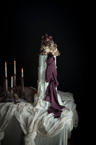 White wedding cake with purple noir ribbon decor on a table against a dark background
