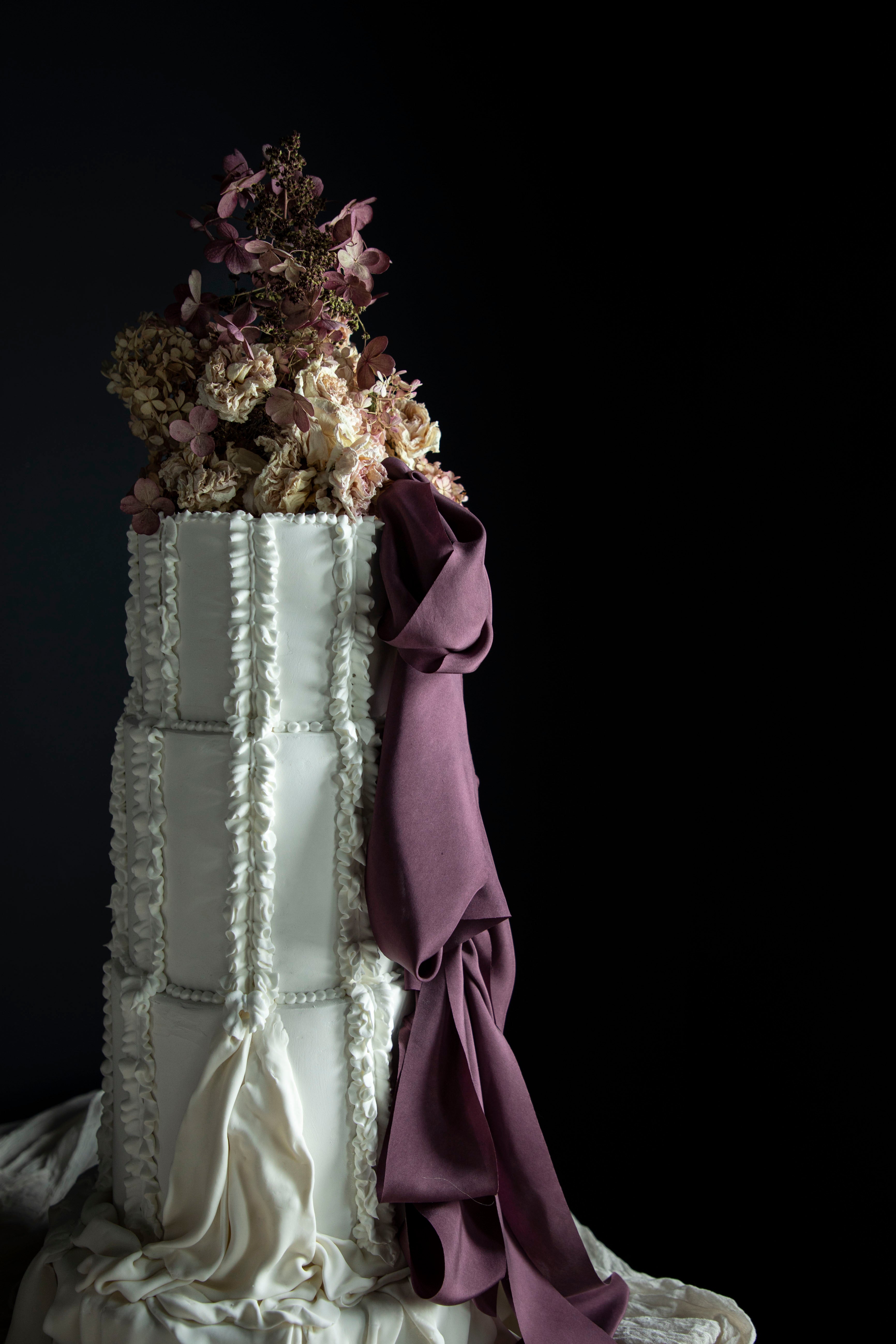 Decorative cake with white frosting, purple ribbon, and floral elements on a black background