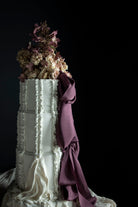 Decorative cake with white frosting, purple ribbon, and floral elements on a black background