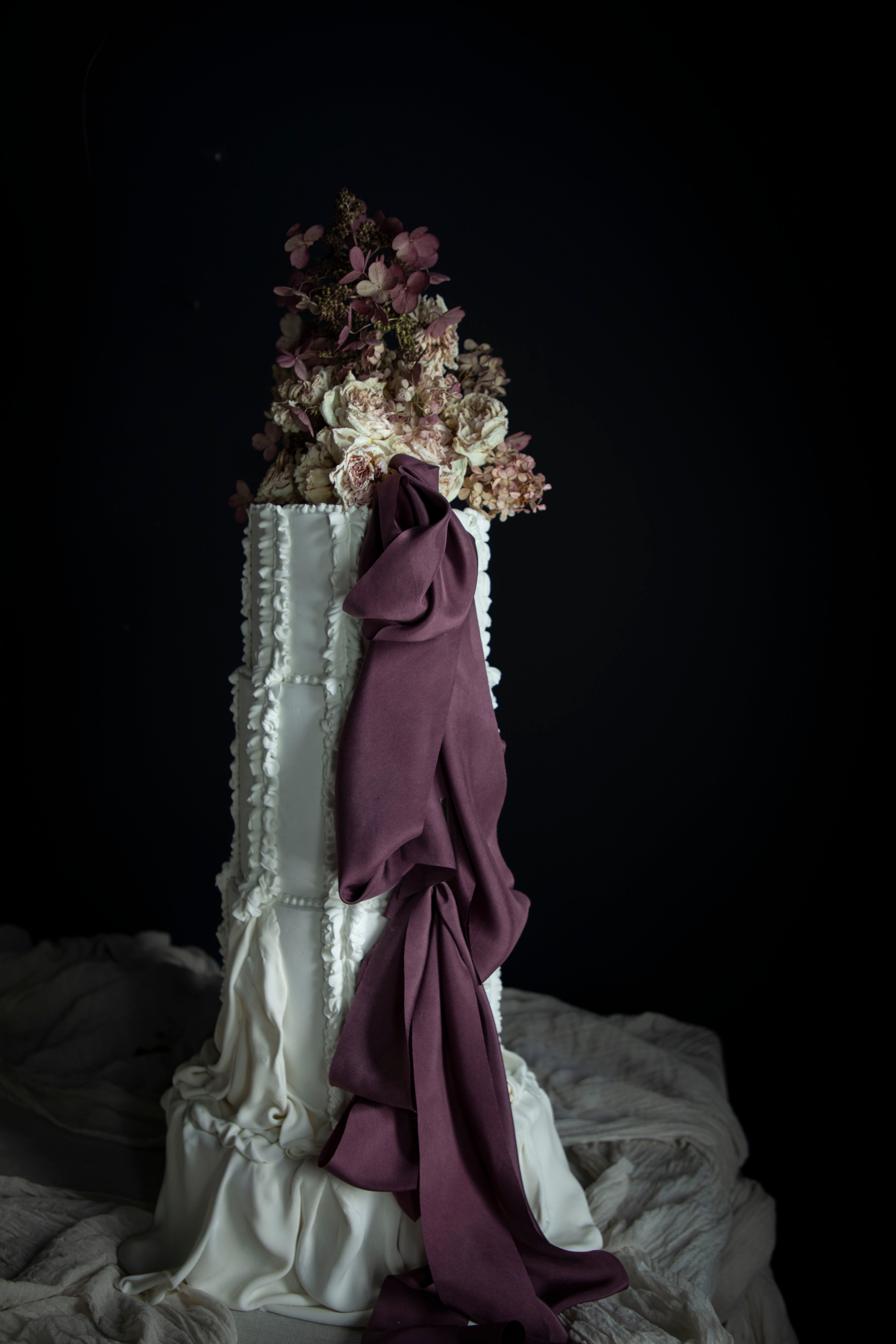 Decorative cake with floral arrangement and plum noir silk ribbon against a dark background