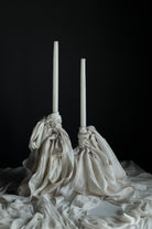 Two white candles in decorative cloth holders on a dark background