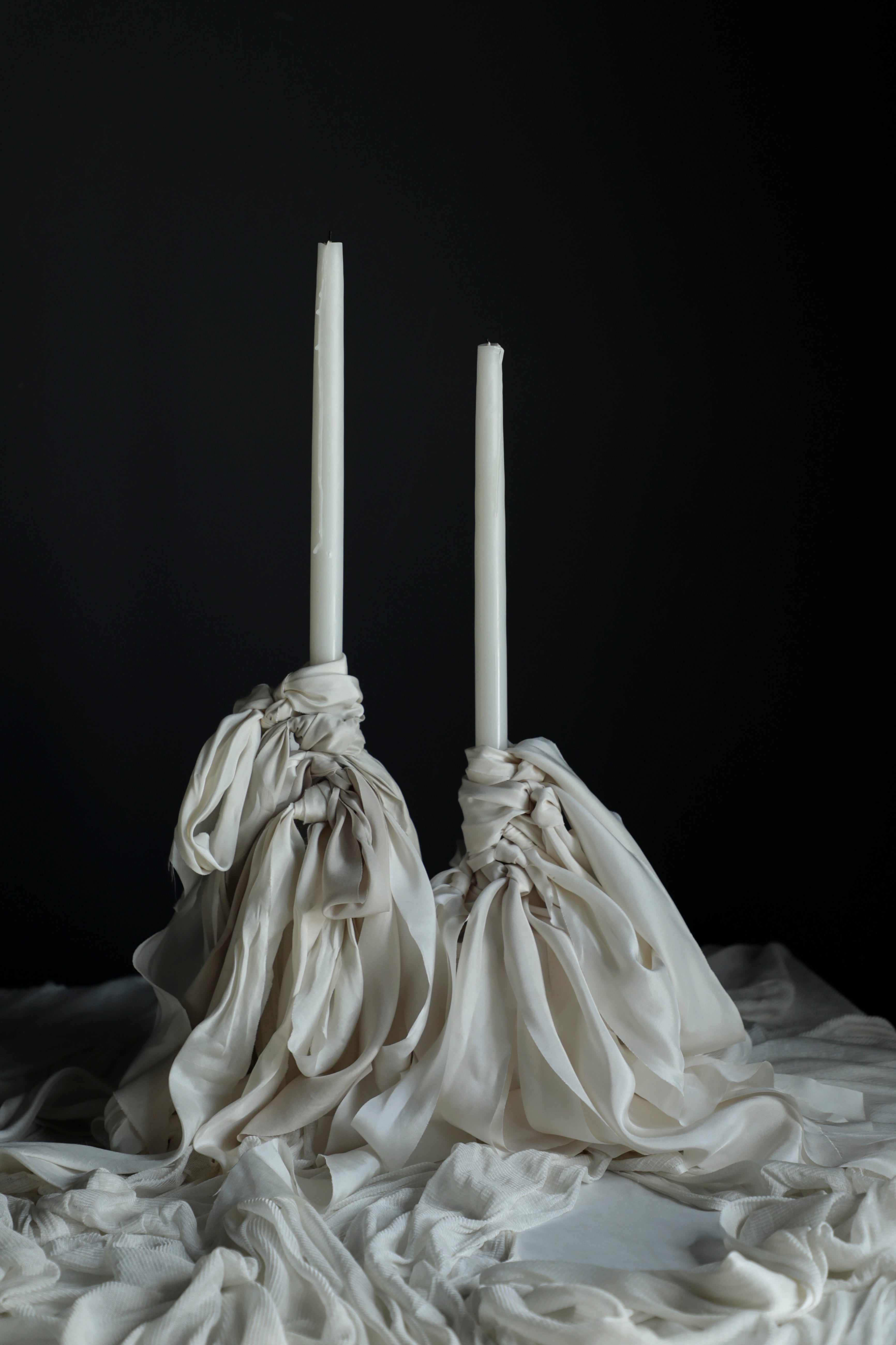Two white candles in decorative cloth holders on a dark background