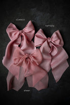 Three pink fabric bows labeled 'classic', 'taffeta', and 'sheer' on a dark background.