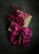 Bouquet of purple flowers with a large pink bow on a dark background