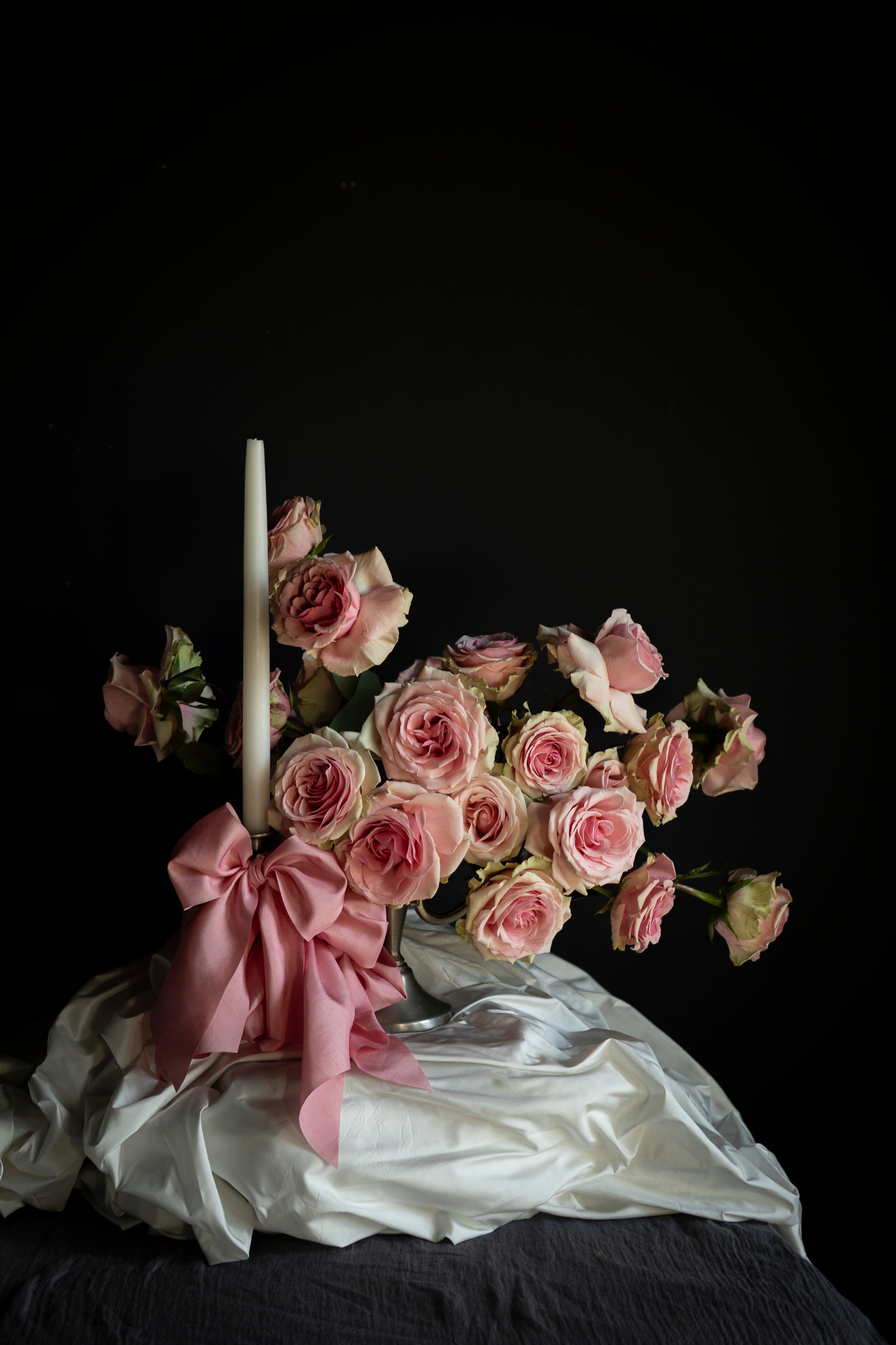 Bouquet of pink roses with a candle and pink ribbon on a dark background
