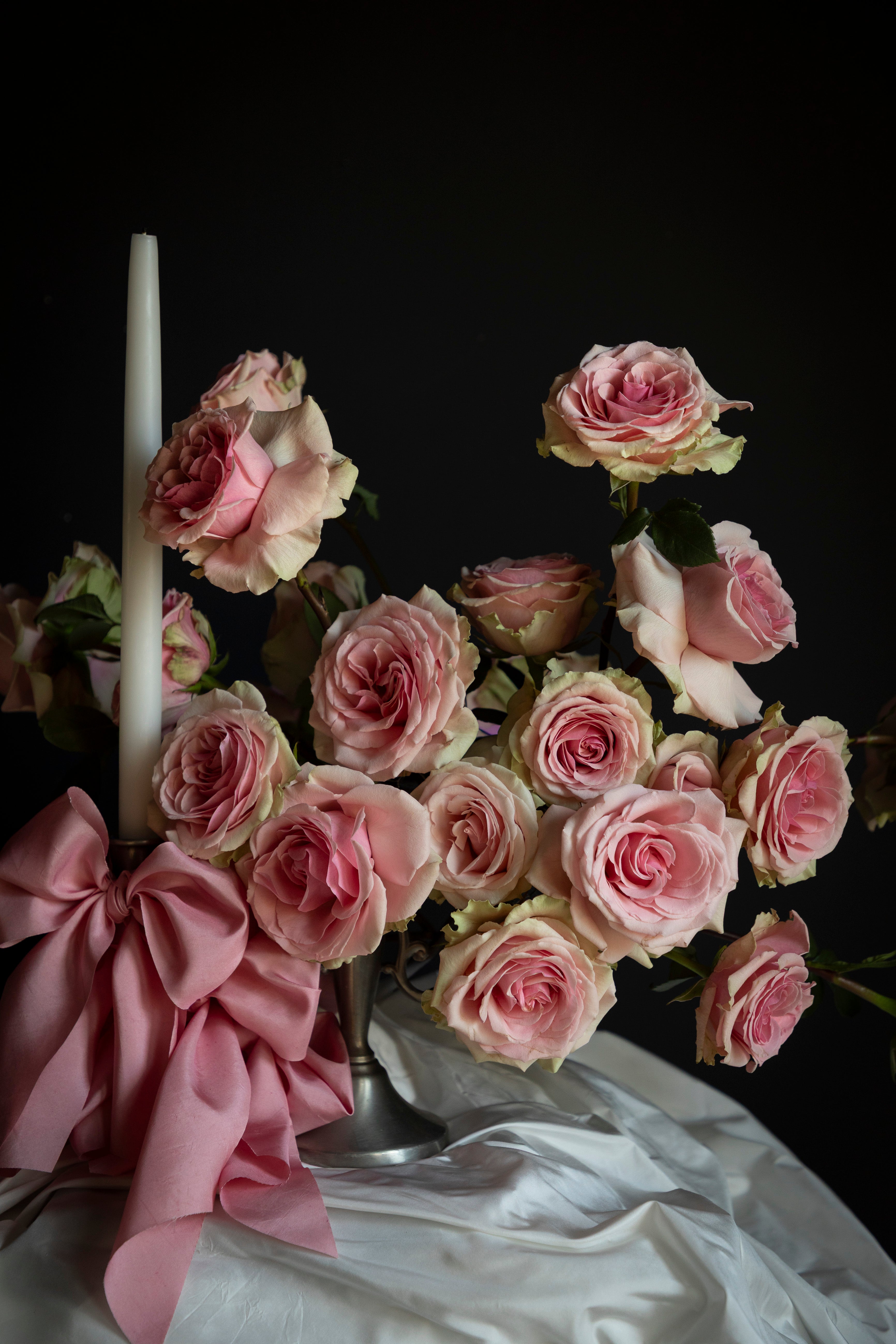 Bouquet of pink roses with a white candle and pink ribbon on a dark background