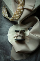 Pearl necklace draped over a beige fabric with a spool of thread and ribbon on a gray surface.
