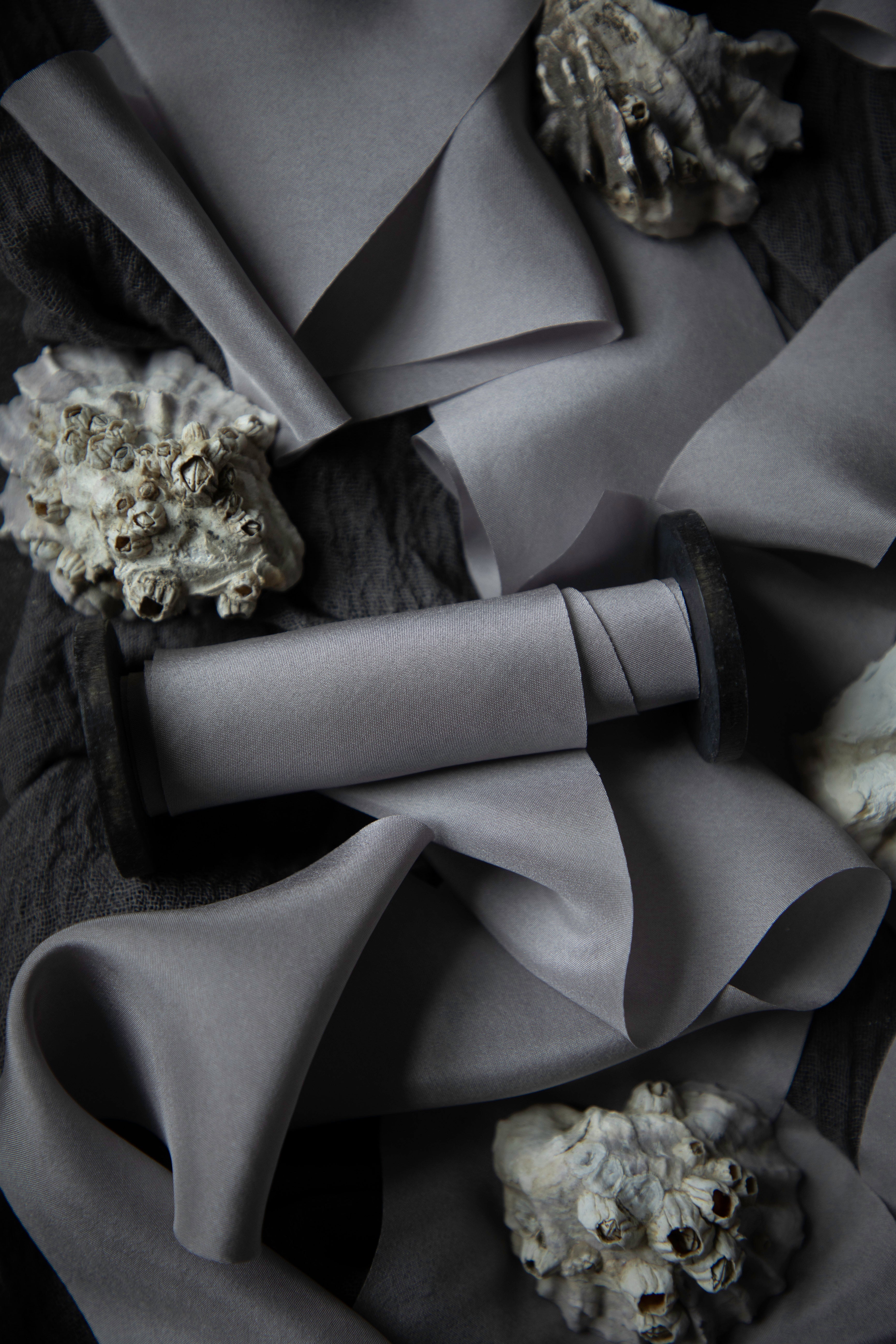 A close-up of draped gray silk ribbon arranged on a dark textured background, with small shell-like decorative props scattered around.