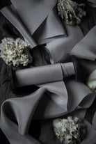 A close-up of draped gray silk ribbon arranged on a dark textured background, with small shell-like decorative props scattered around.