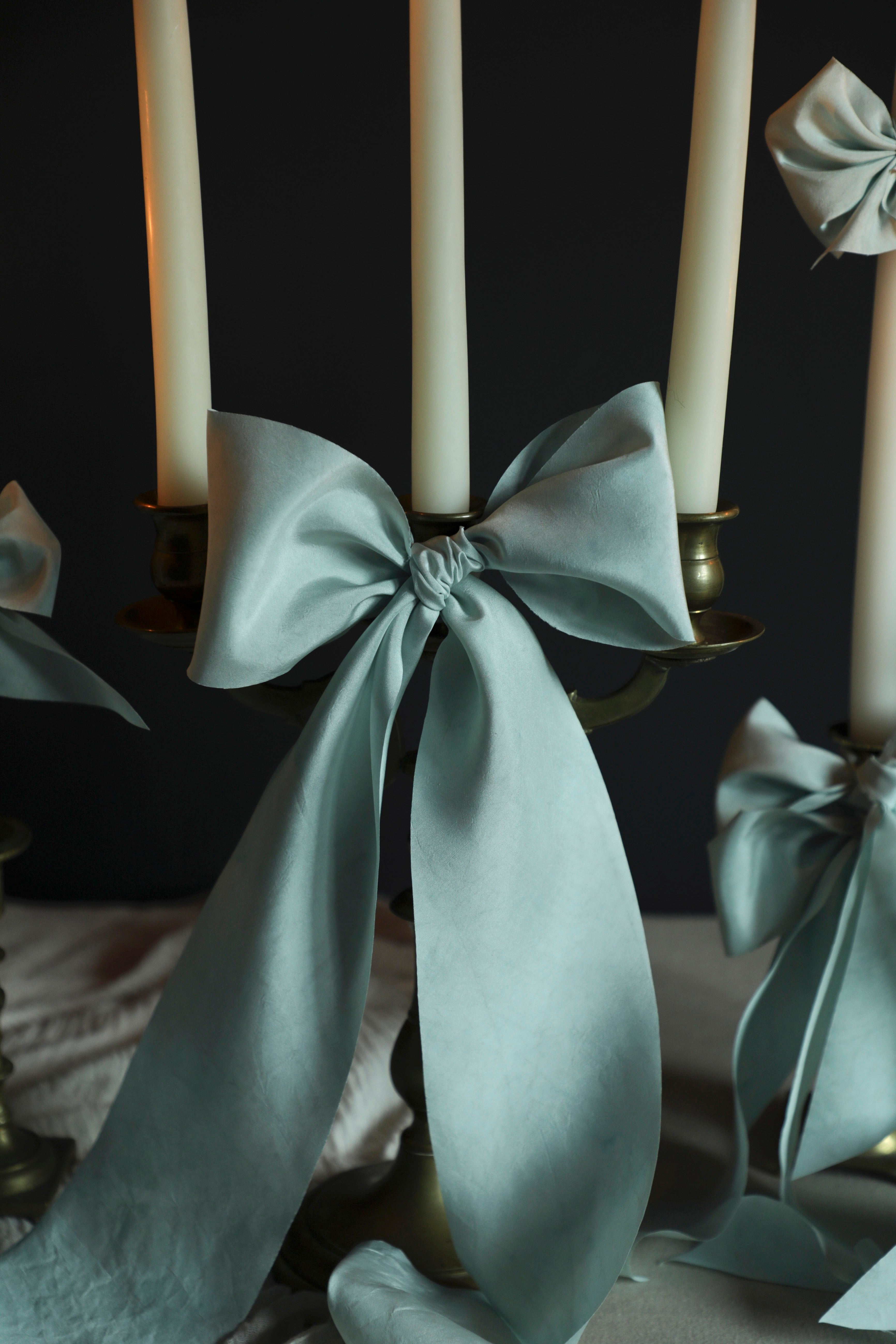 Candle holder with light indigo blue silk ribbons and candles against a dark background