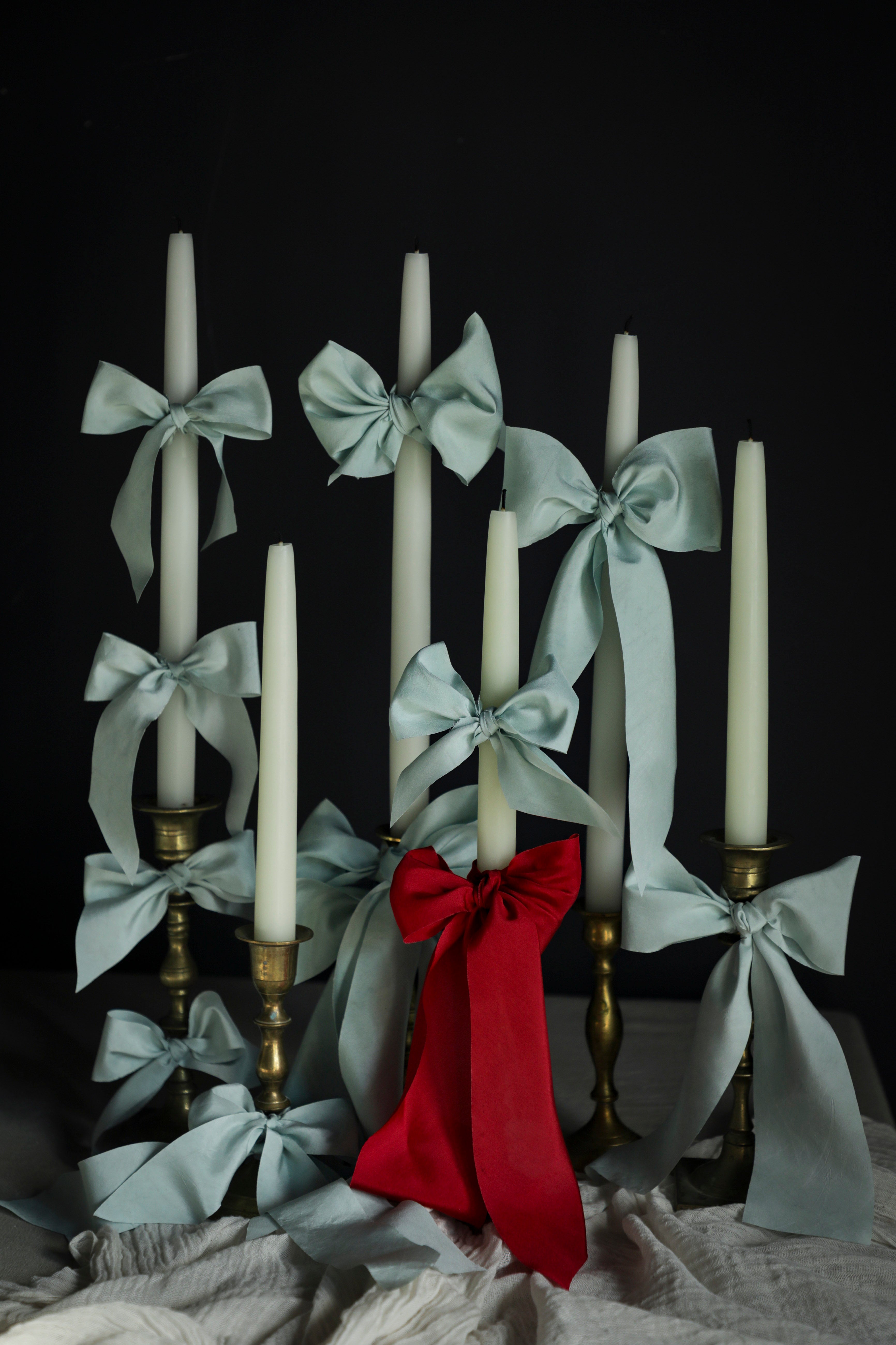 Candle holder with white candles, Cinderella blue silk ribbons, and a red bow on a dark background