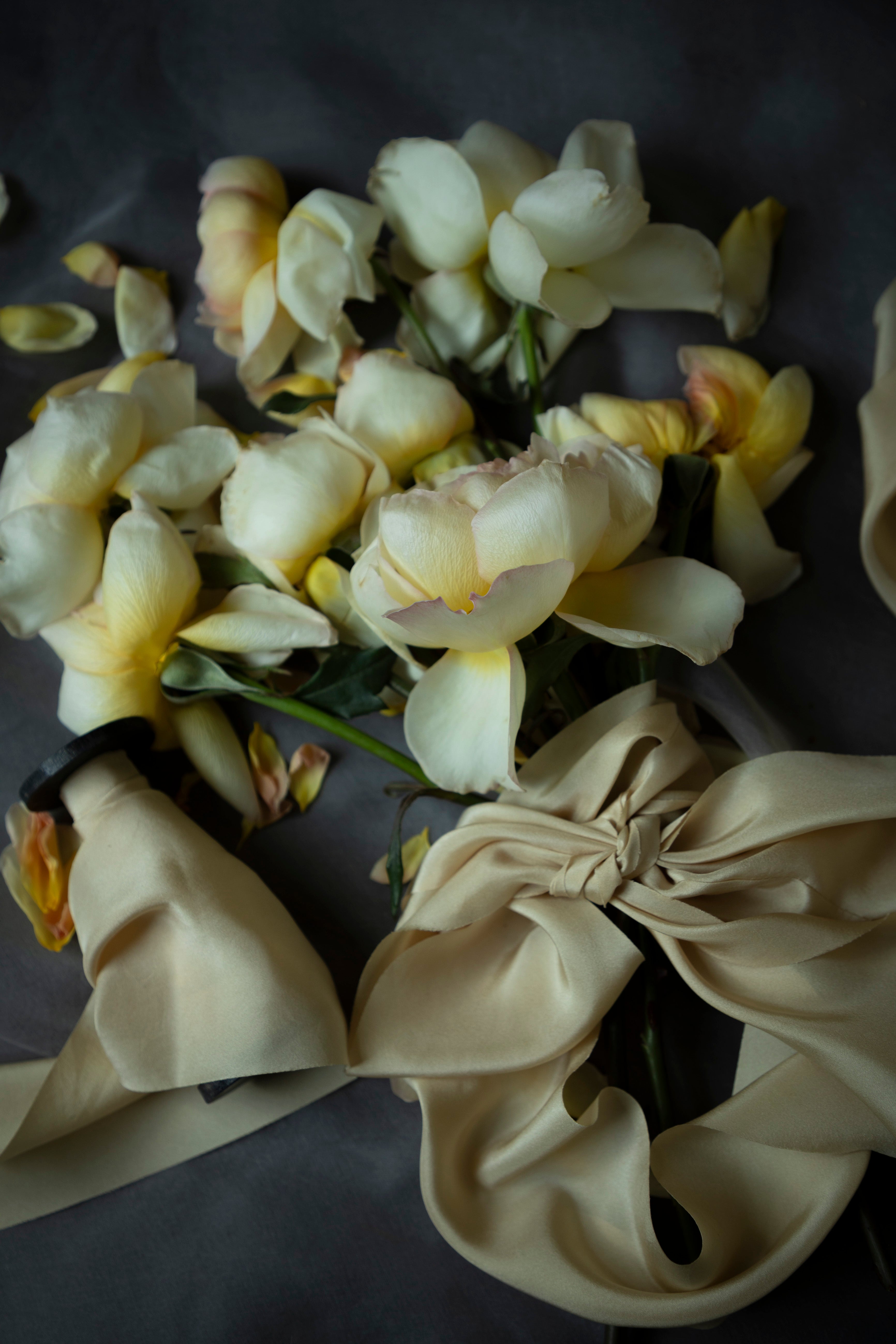 A bouquet of pale cream and yellow flowers tied with a matching cream yellow ribbon, arranged on a dark gray background.