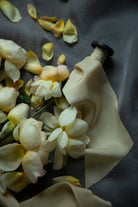 A antique gold silk ribbon spool with a black wood spool, shown with draped fabric and scattered pale yellow flower petals on a dark gray background.