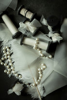 antique white wedding ribbon for florists. Displayed on a flatlay with white feather and pearls.