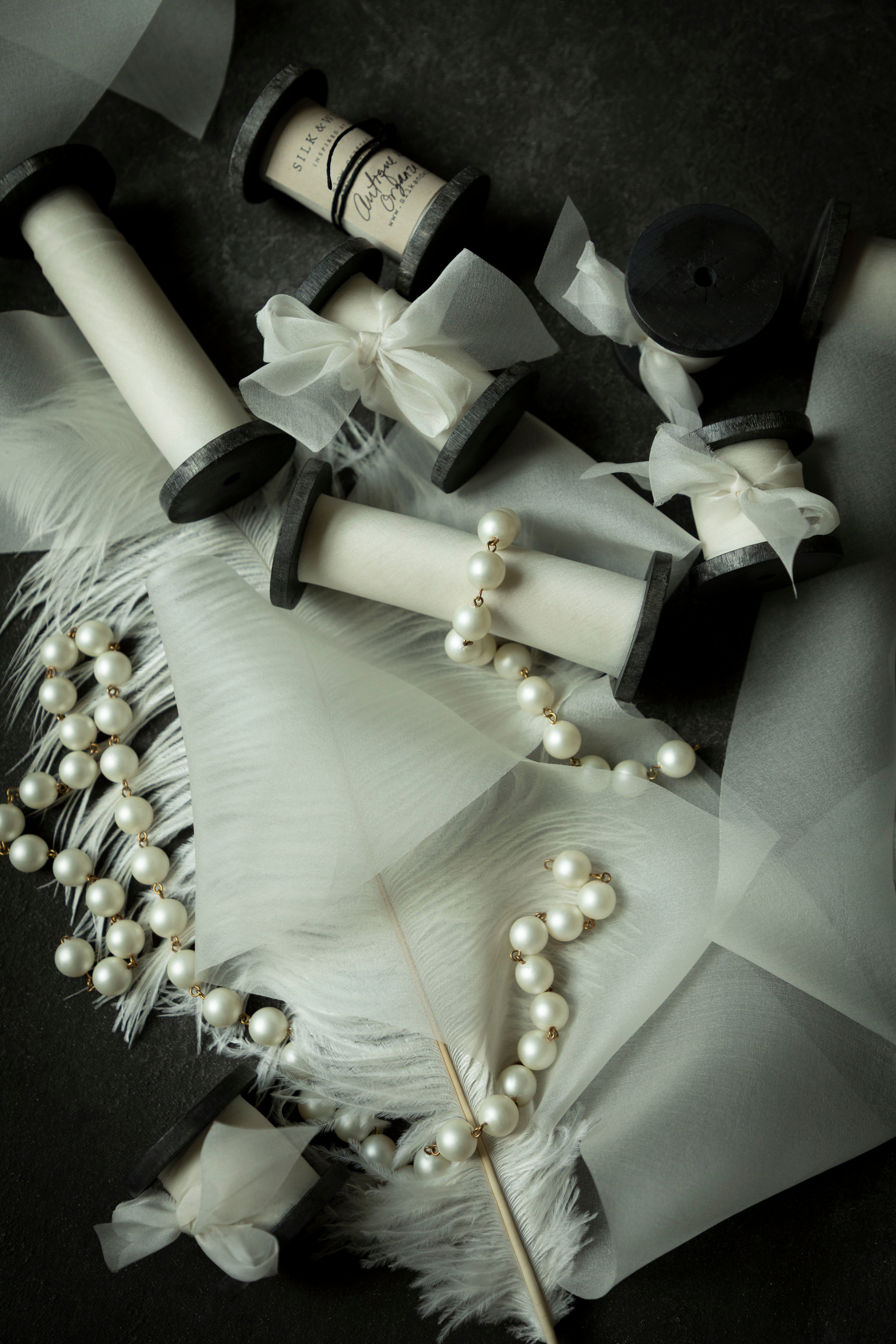 antique white wedding ribbon for florists. Displayed on a flatlay with white feather and pearls.