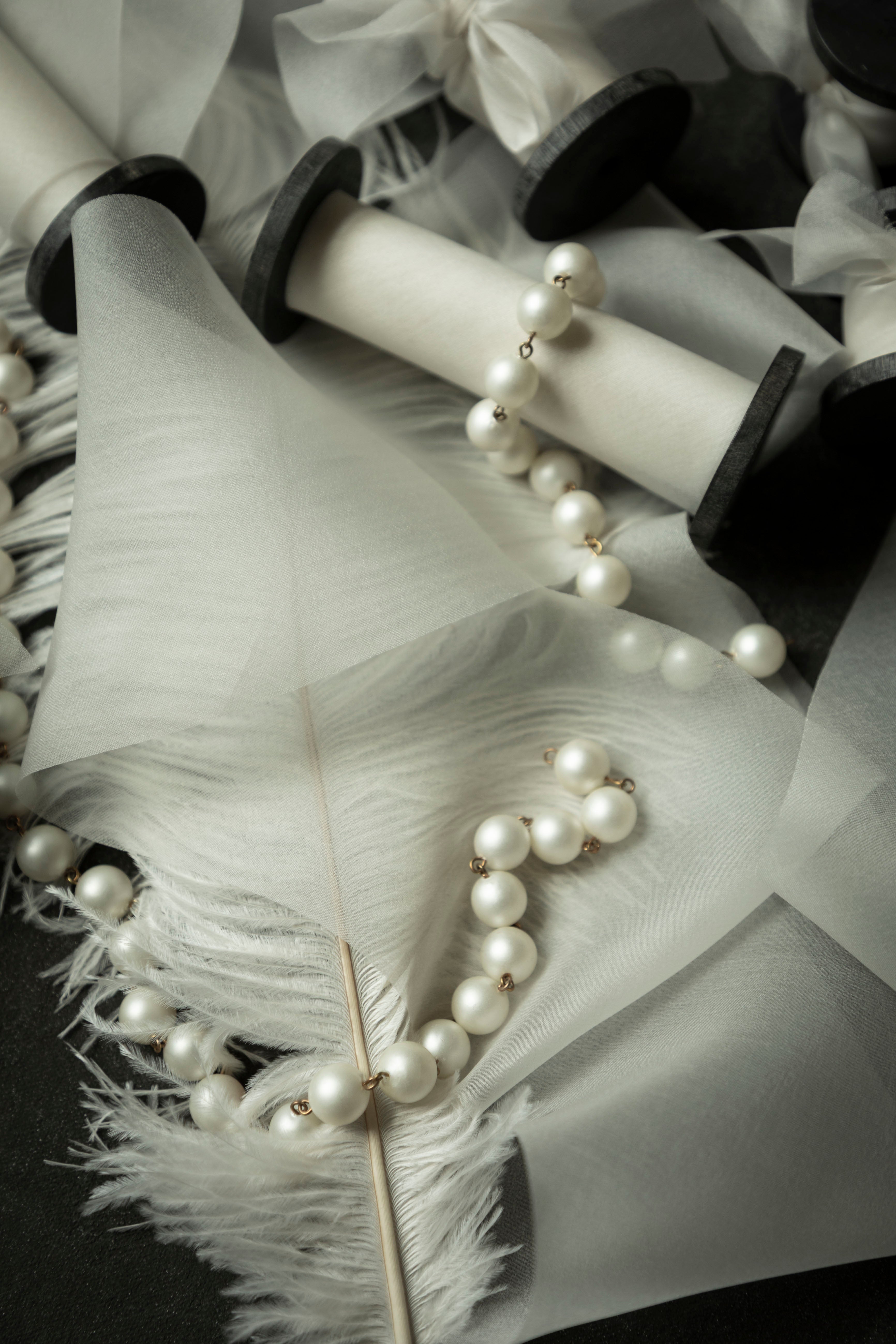 antique white wedding ribbon for florists. Displayed on a flatlay with white feather and pearls.