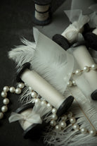 close-up of antique white wedding ribbon for florists. Displayed on a flatlay with white feather and pearls.