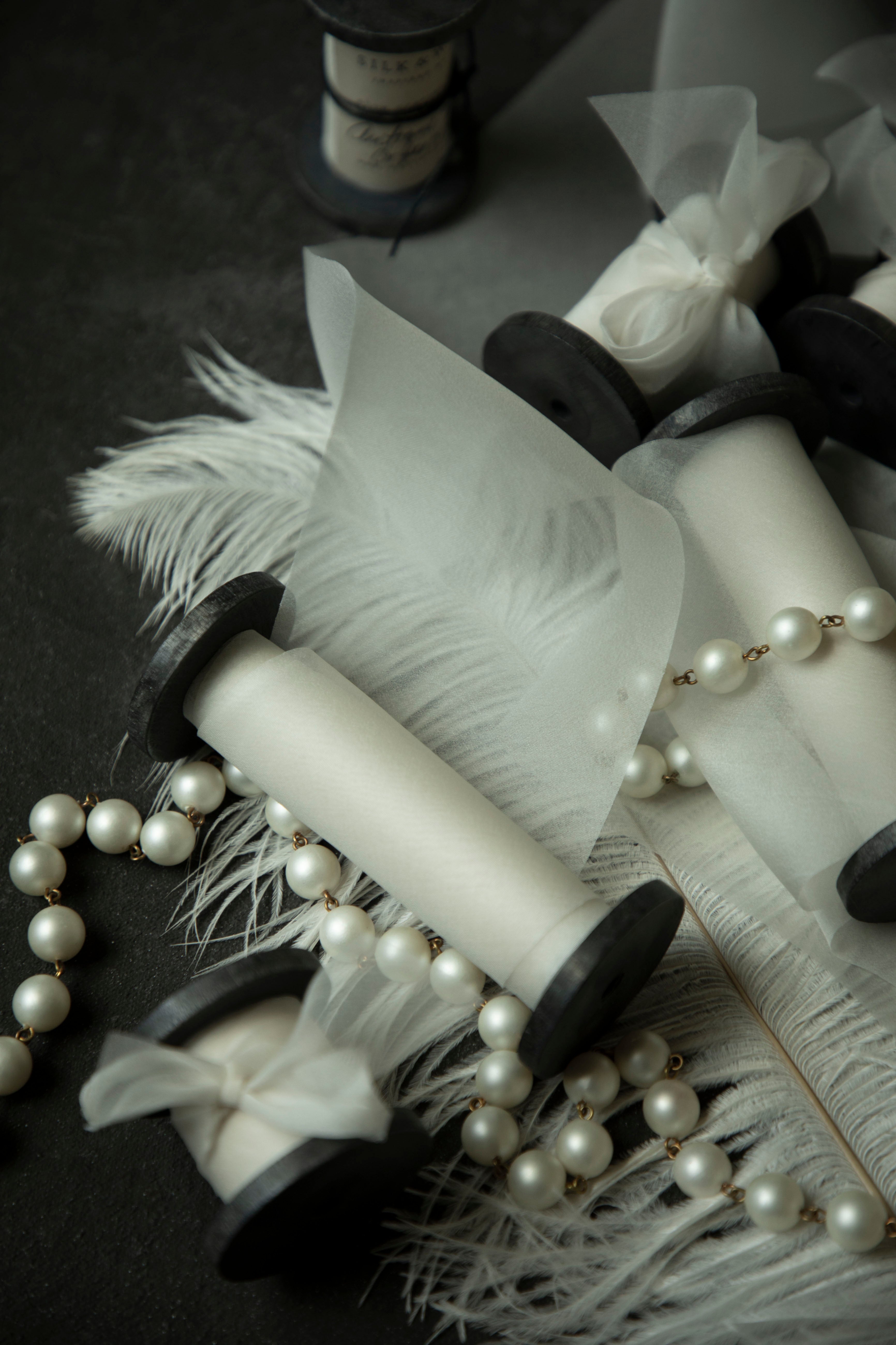 close-up of antique white wedding ribbon for florists. Displayed on a flatlay with white feather and pearls.