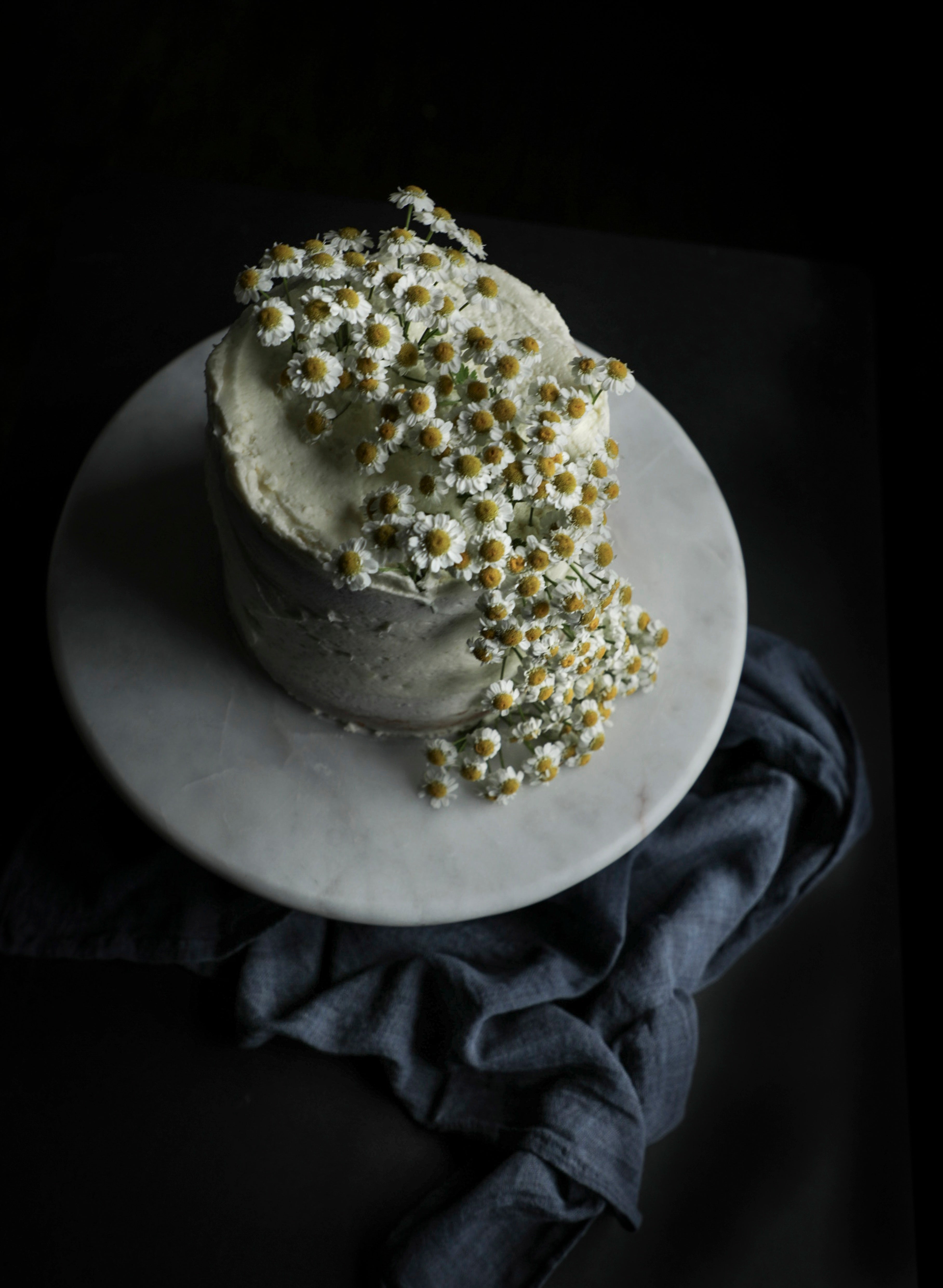 Two-tiered cake with white frosting and floral decorations on a dark background
