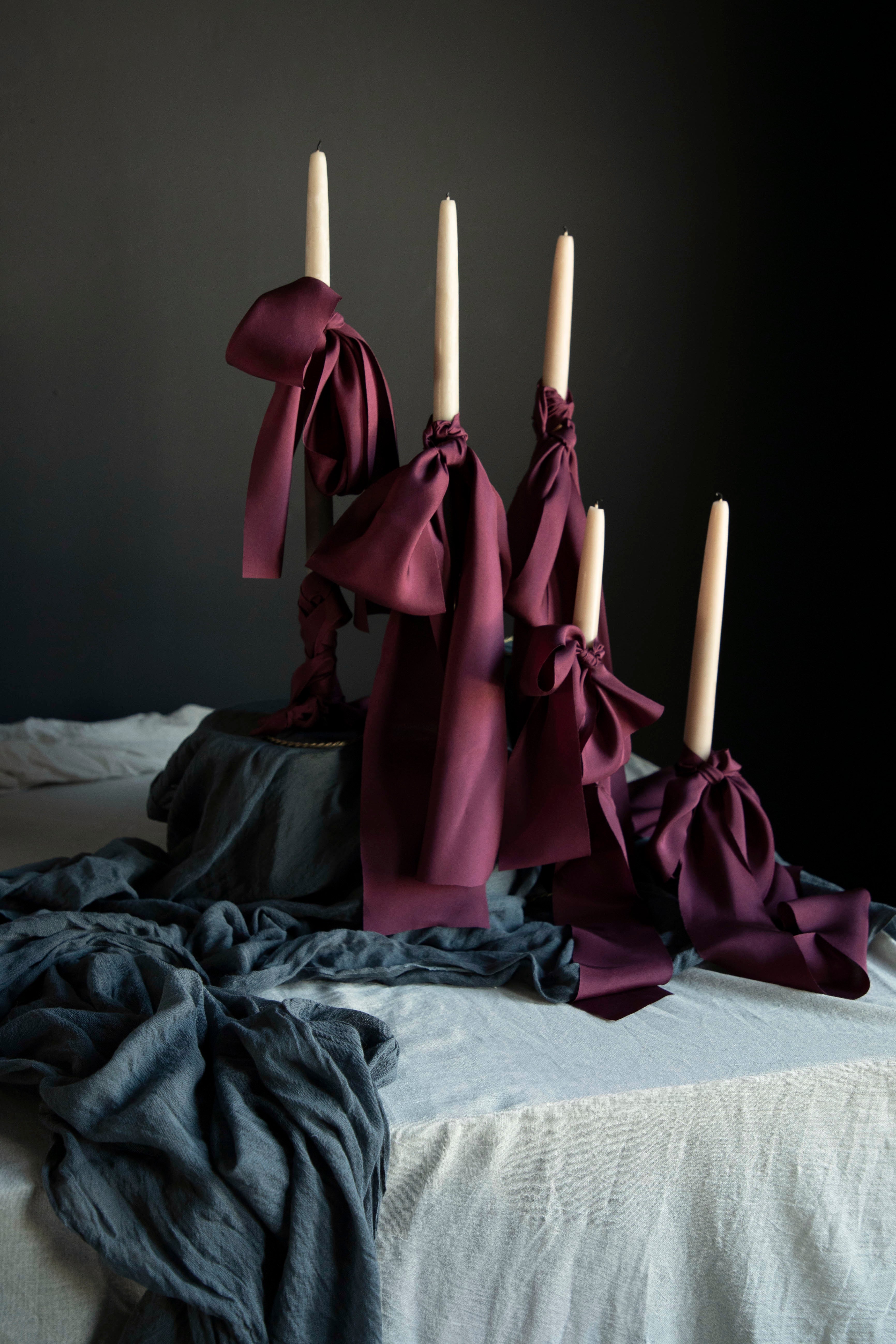 Decorative candles with ribbons on a table with draping textiles