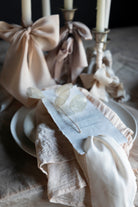 Decorative table setting with white candles, ribbons, and a small dish on a wooden surface.