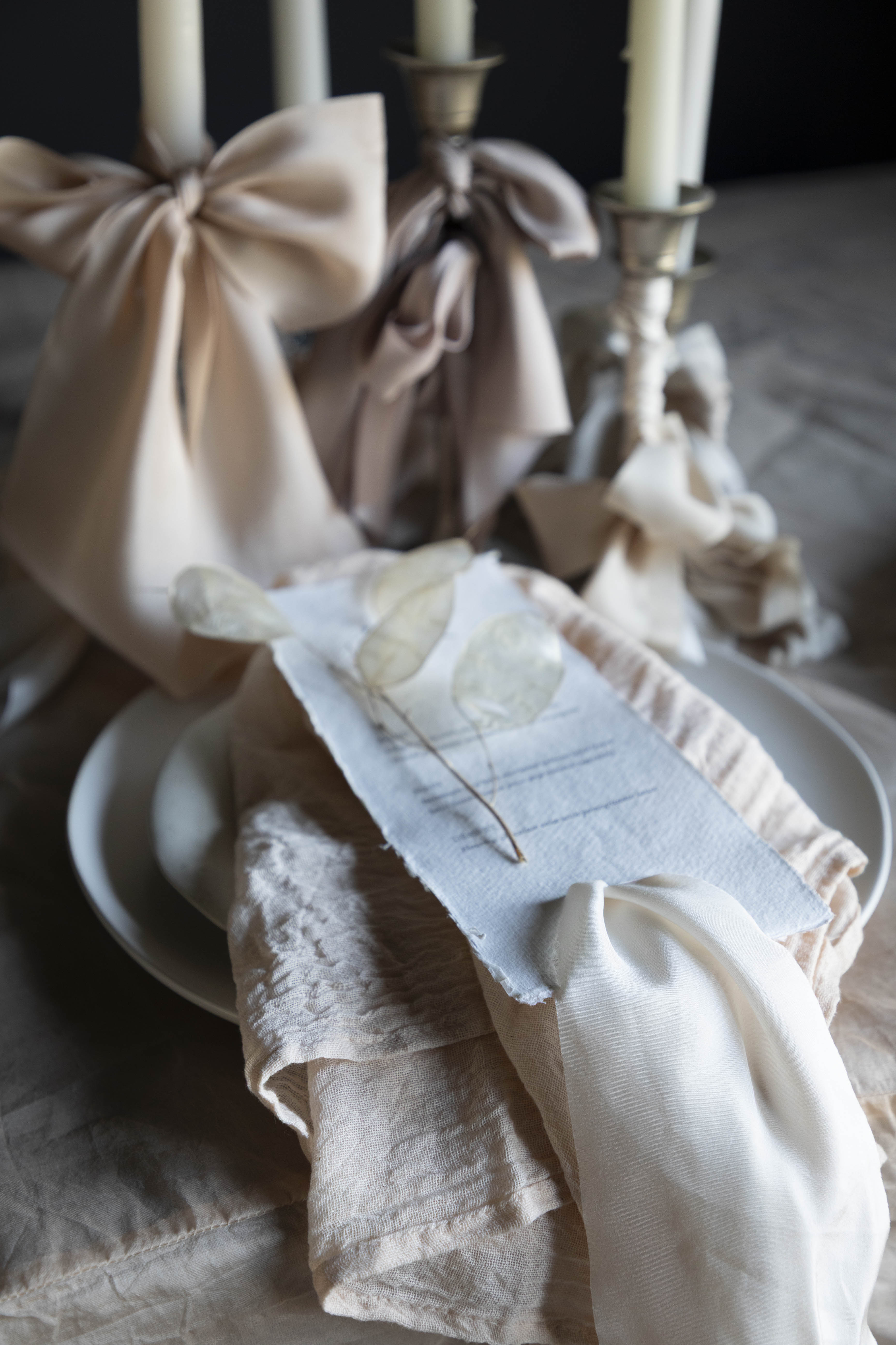 Decorative table setting with white candles, ribbons, and a small dish on a wooden surface.