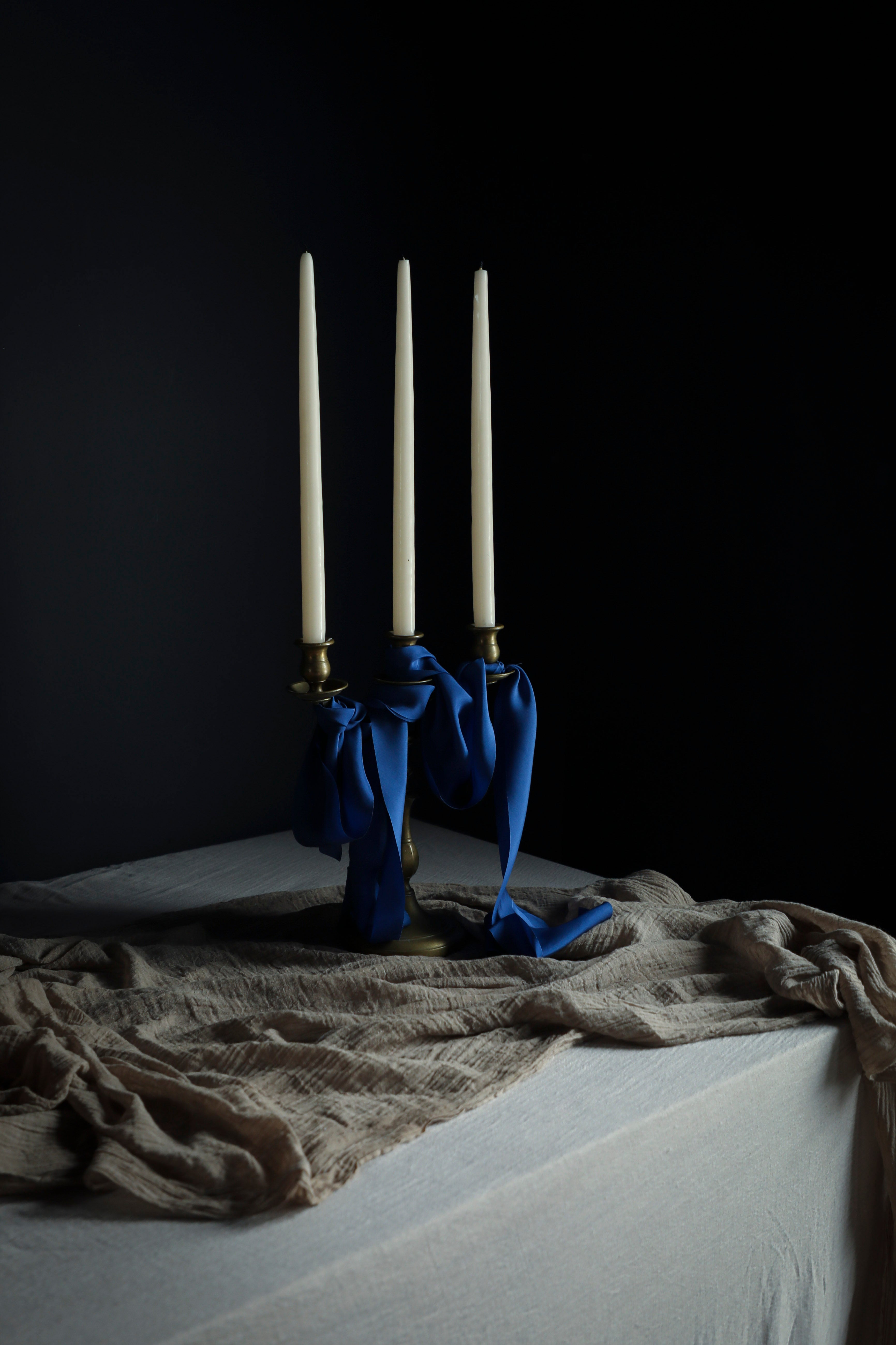 Three candles in a holder with blue ribbons on a dark surface