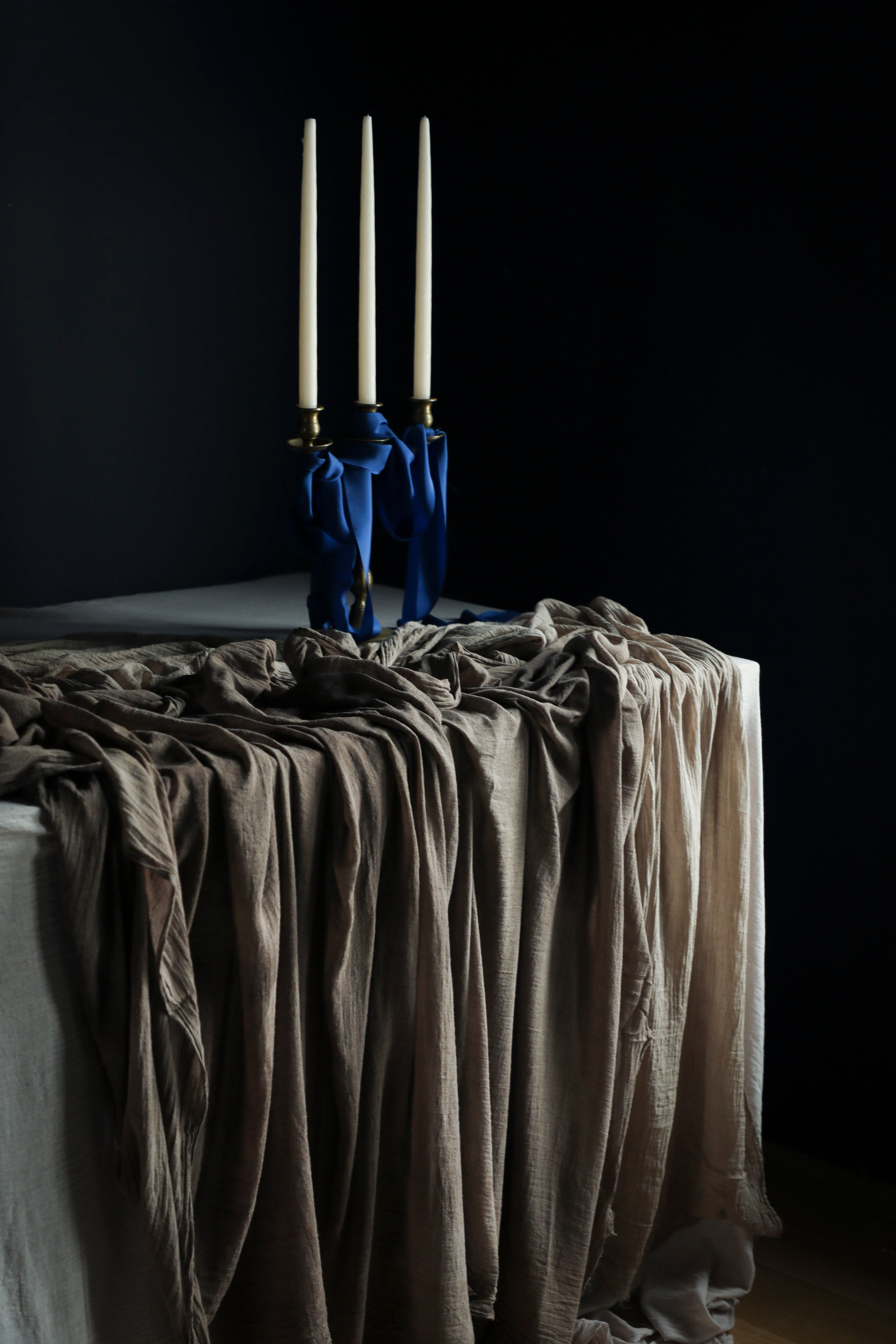 Candle holder with three candles on a draped tablecloth against a dark background