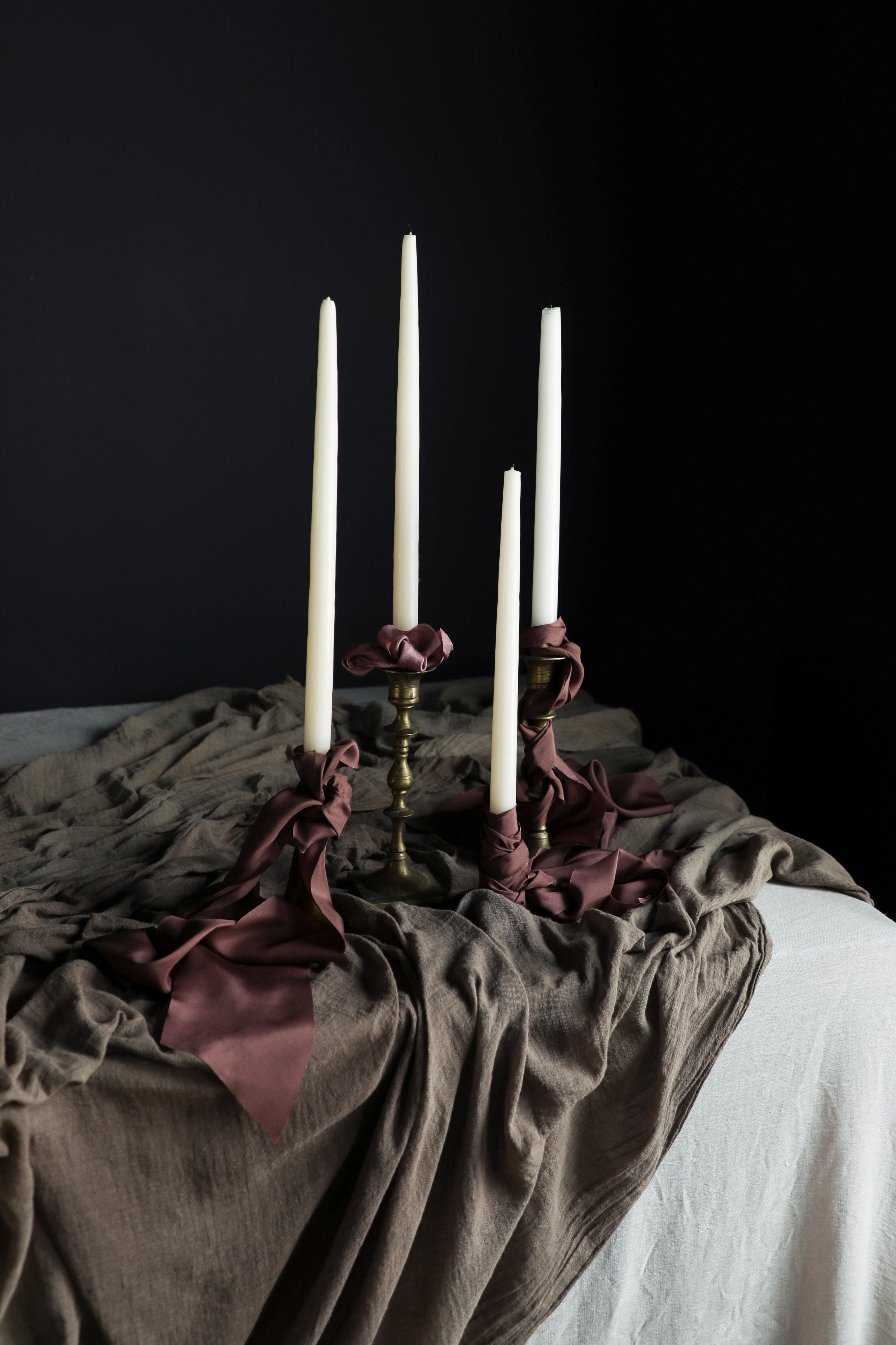 Three candles on ornate candlesticks with draped fabric against a dark background