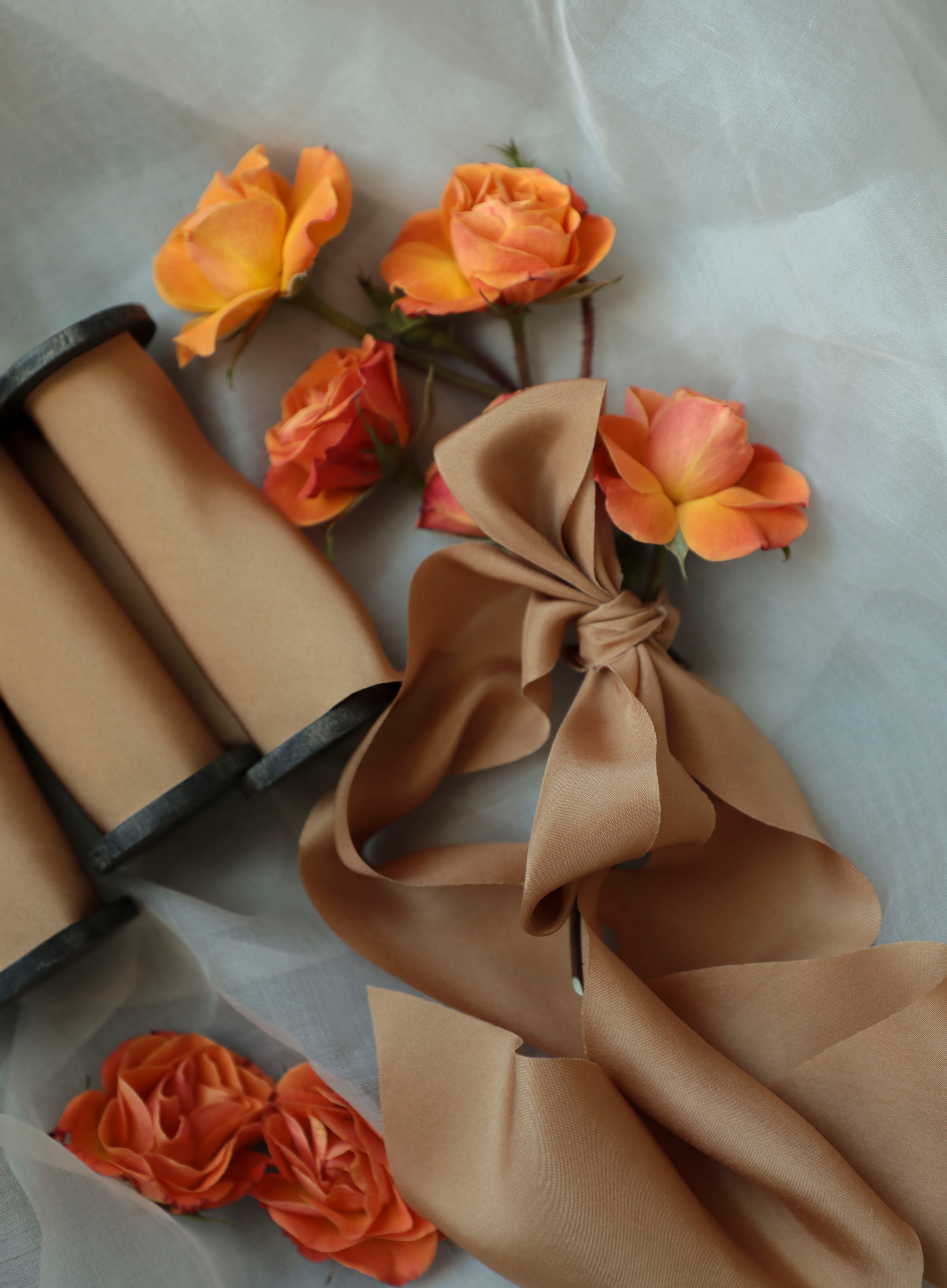 Ribbons on wood spools with orange flowers and a bow on a light background