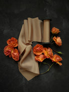 Spool of coral silk ribbon with orange roses on a dark background
