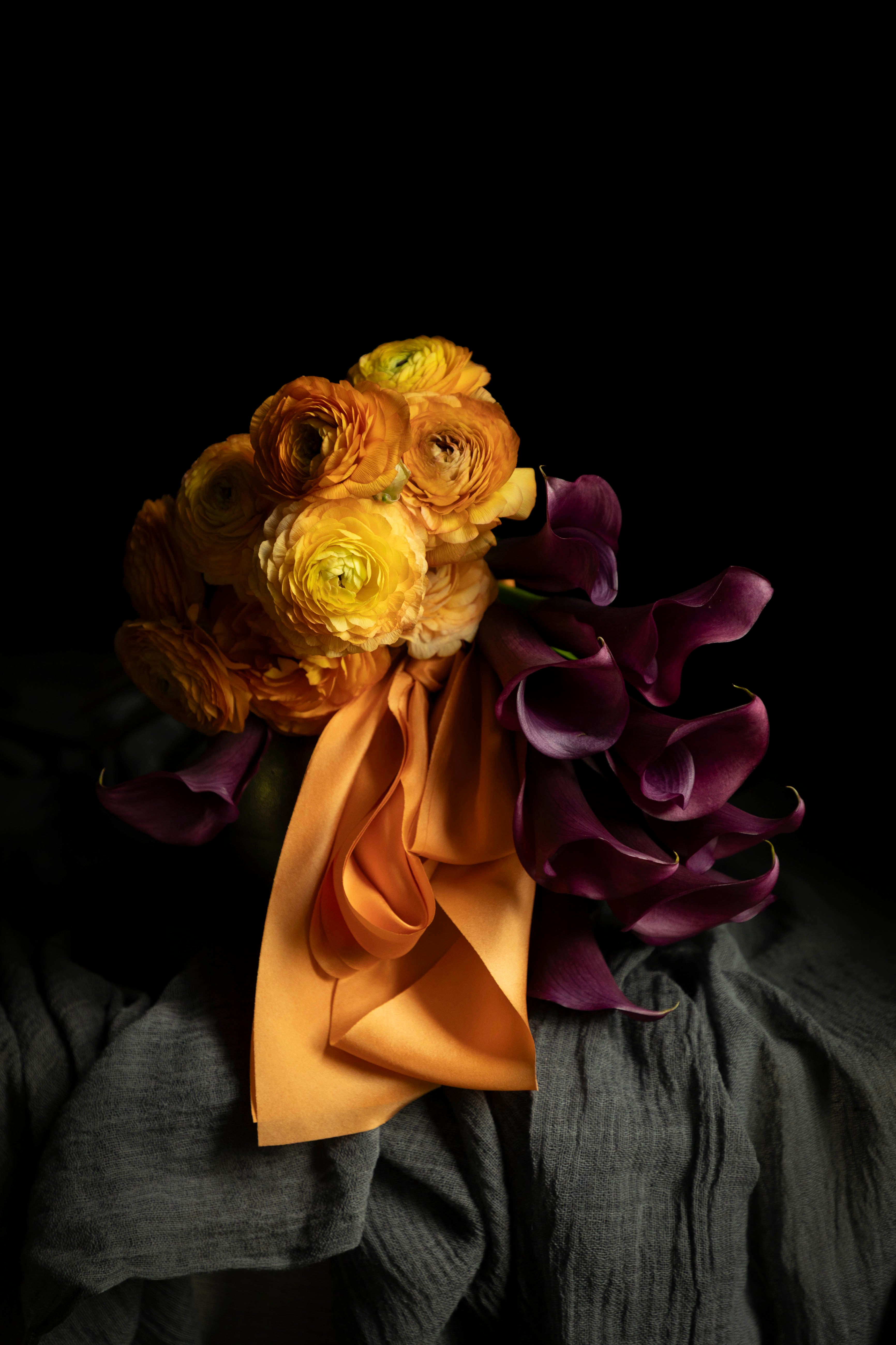 Orange ranunculus and purple calla lilies flower arrangement with orange silk ribbon