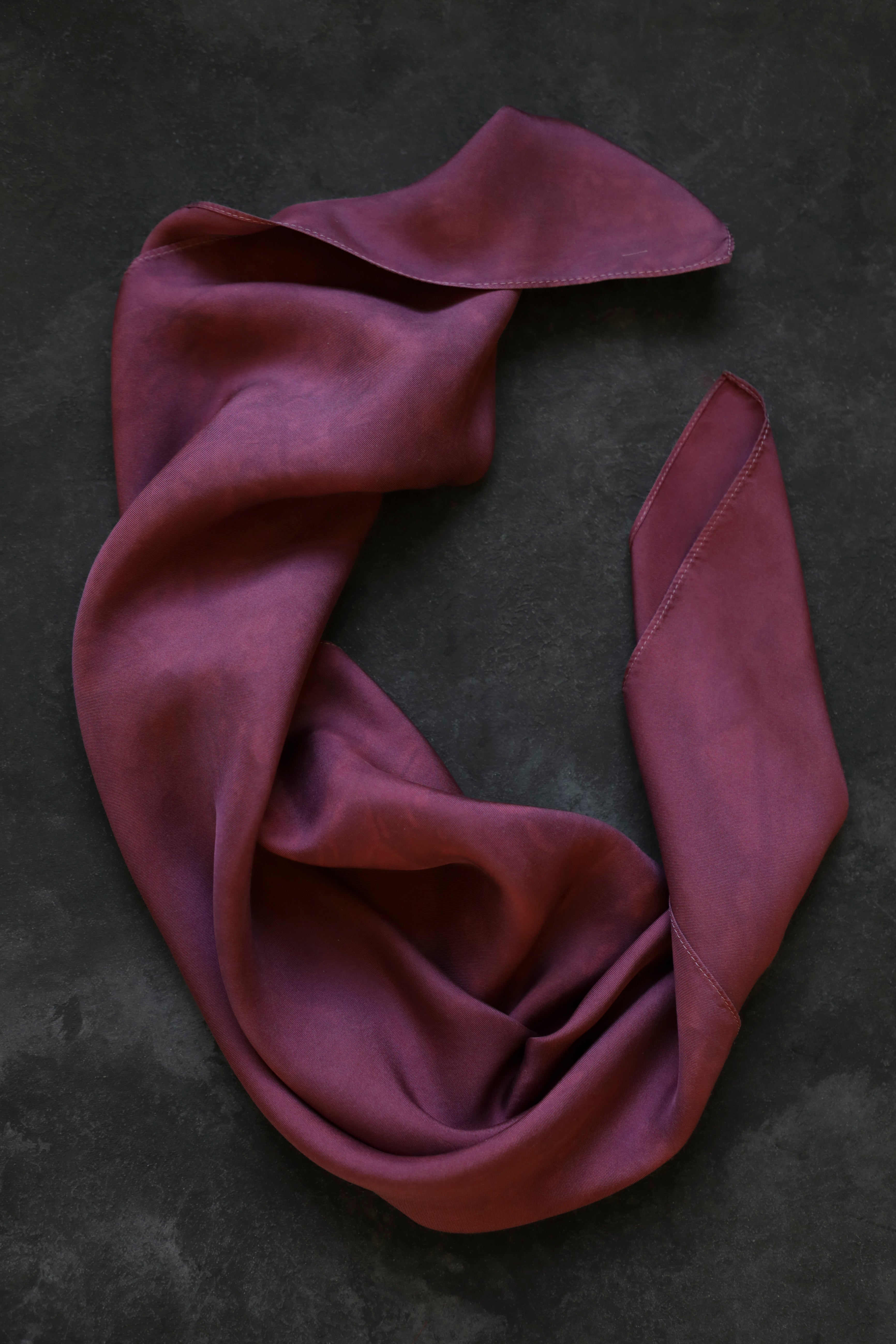 A dusty mauve-purple scarf draped in soft folds on a dark textured background.