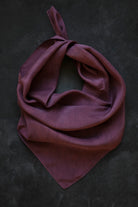 A mauve-purple silk scarf tied in a loose knot, displayed on a dark textured background.
